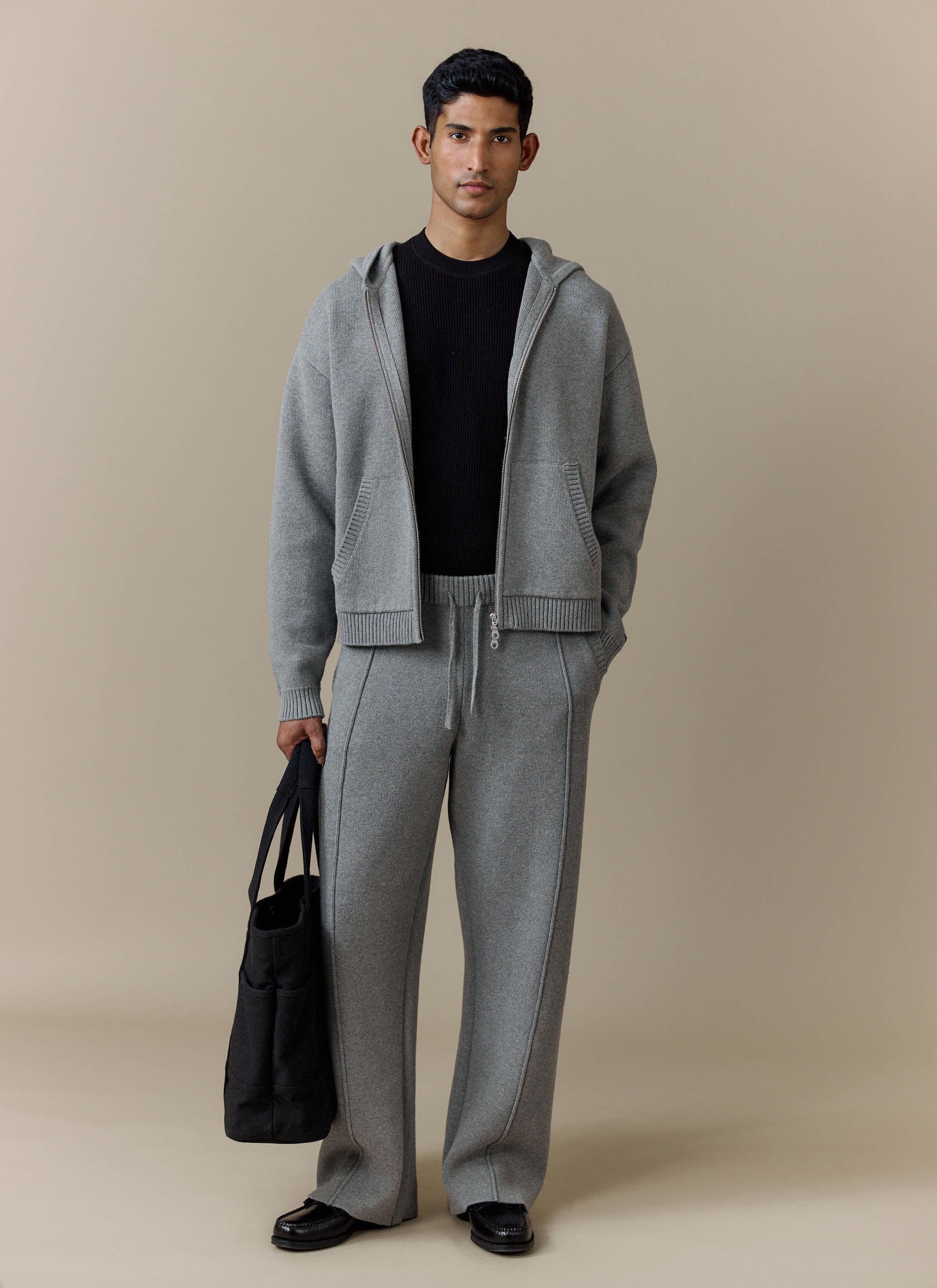 A model wears the Percival Chronicle Knitted Straight Leg Trackpant in grey, styled with the matching zip-up hoodie.