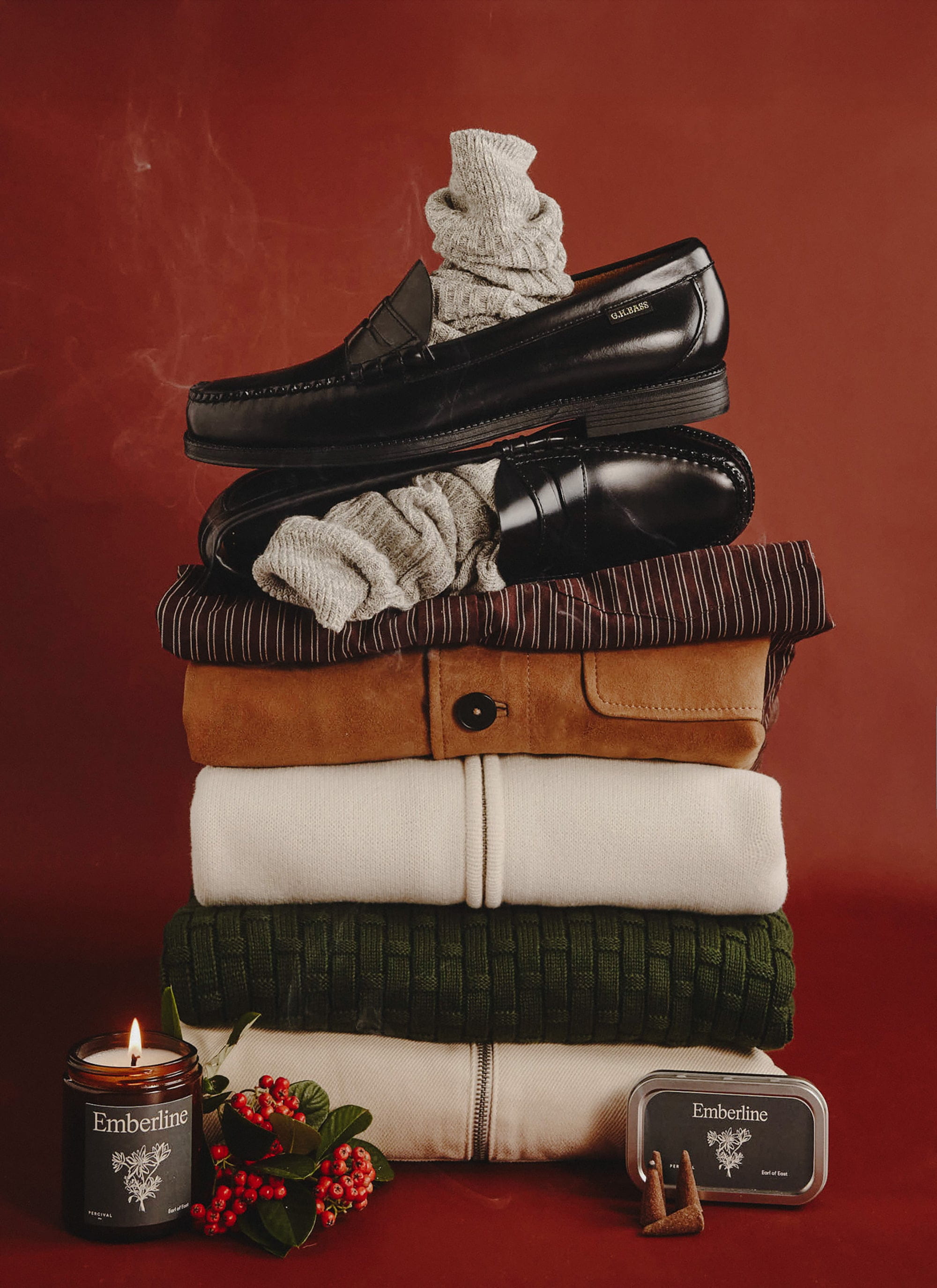 A festive stack of Percival menswear including jumpers, shoes and socks, with an Emberline candle and incense cones.