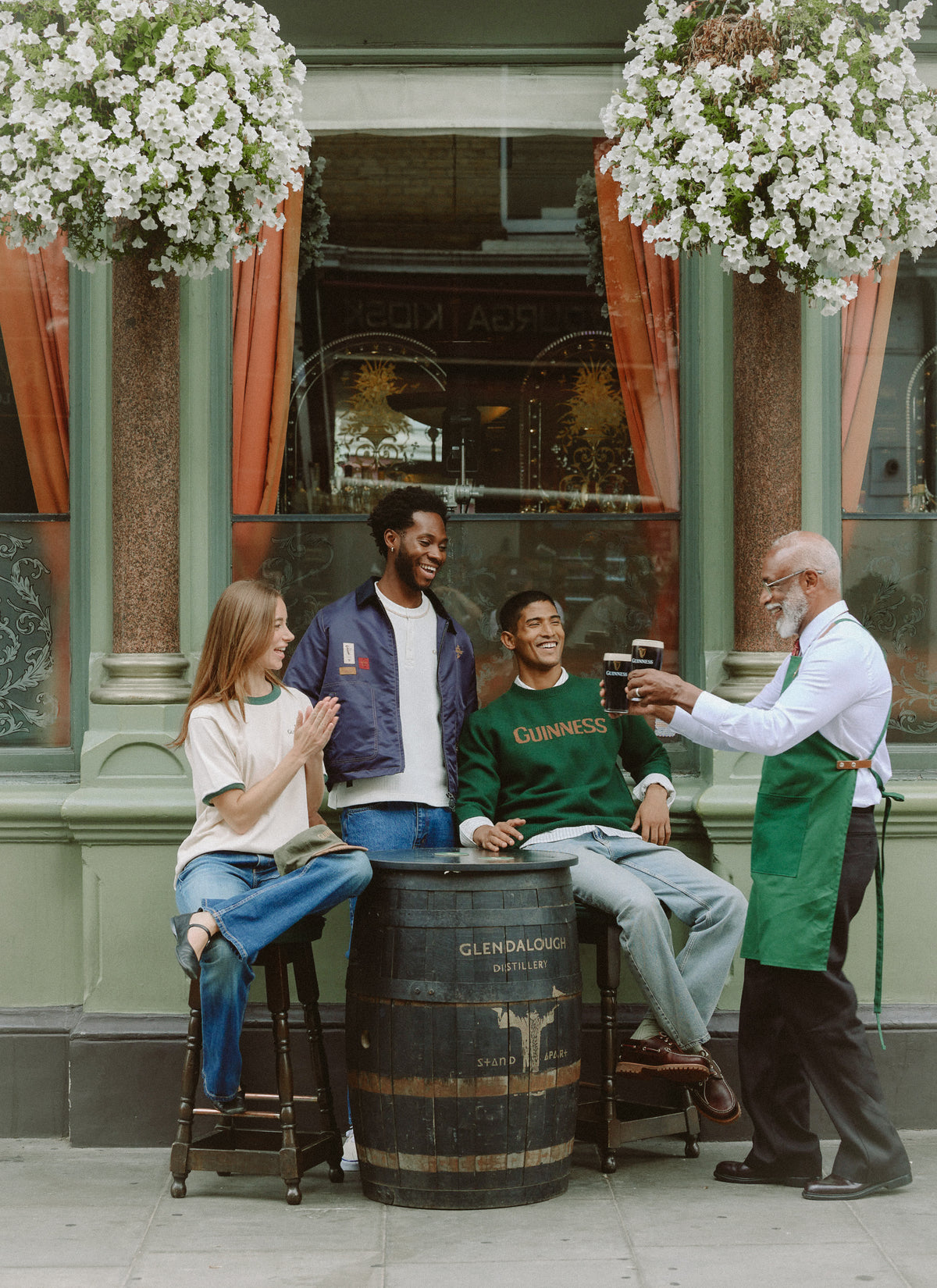 Models and pub worker enjoying pints outside The George, featuring the Guinness x Percival forest green merino wool jumper.