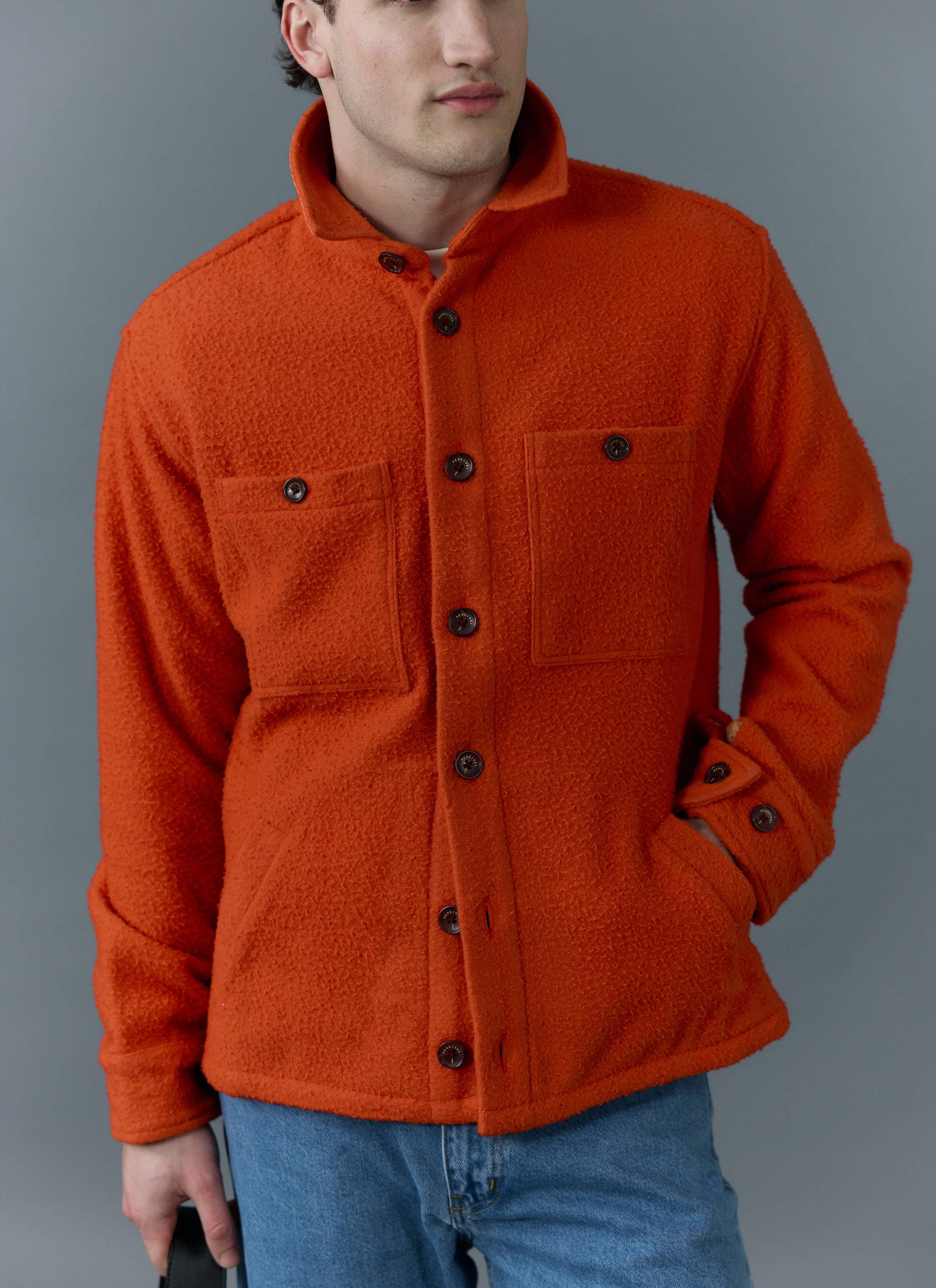 A model wears the Percival orange Casentino wool Blanket Overshirt with blue jeans against a grey background.