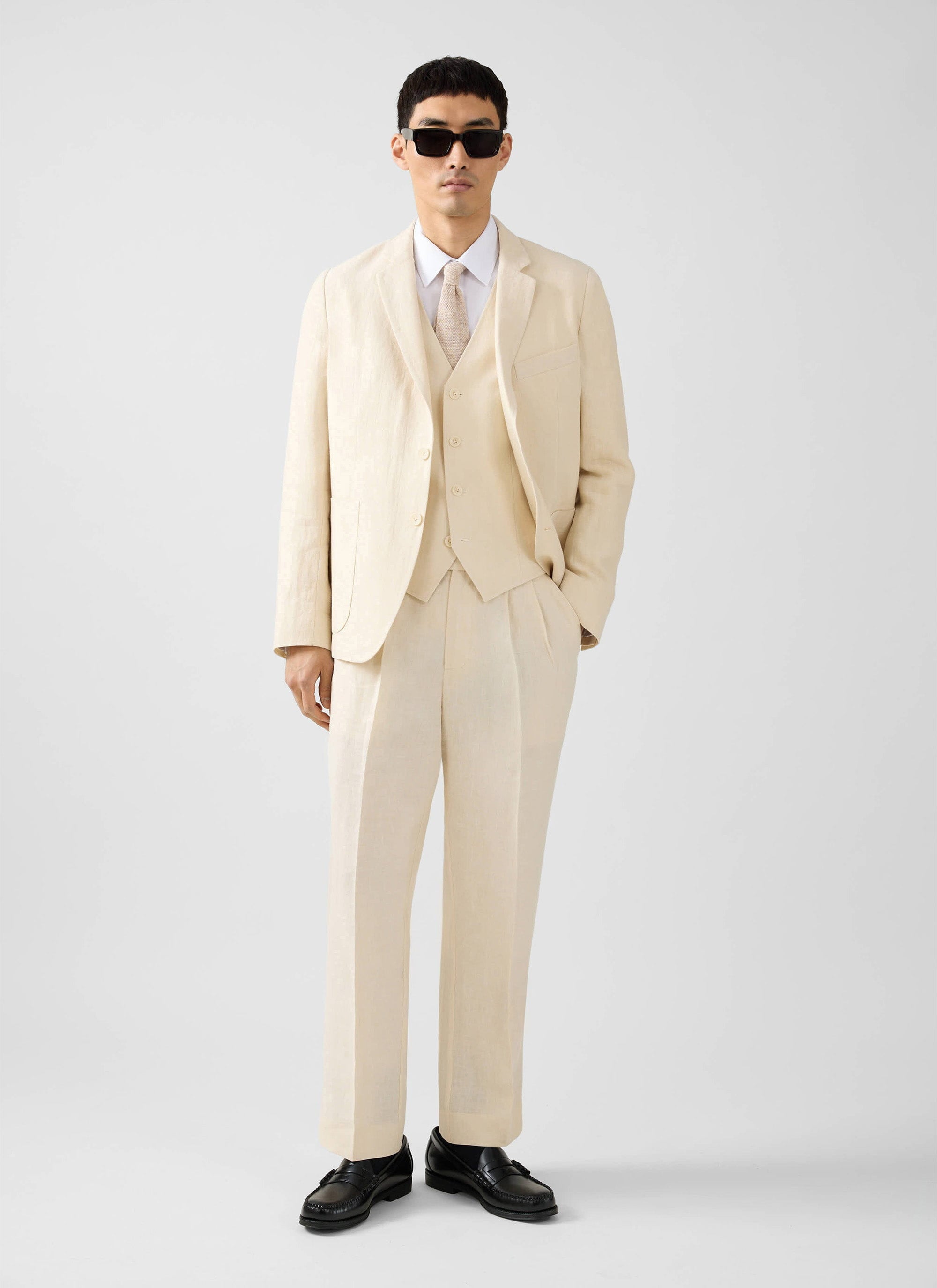 A model wears the Percival cream linen waistcoat, styled with the matching suit trousers, blazer, and sunglasses.