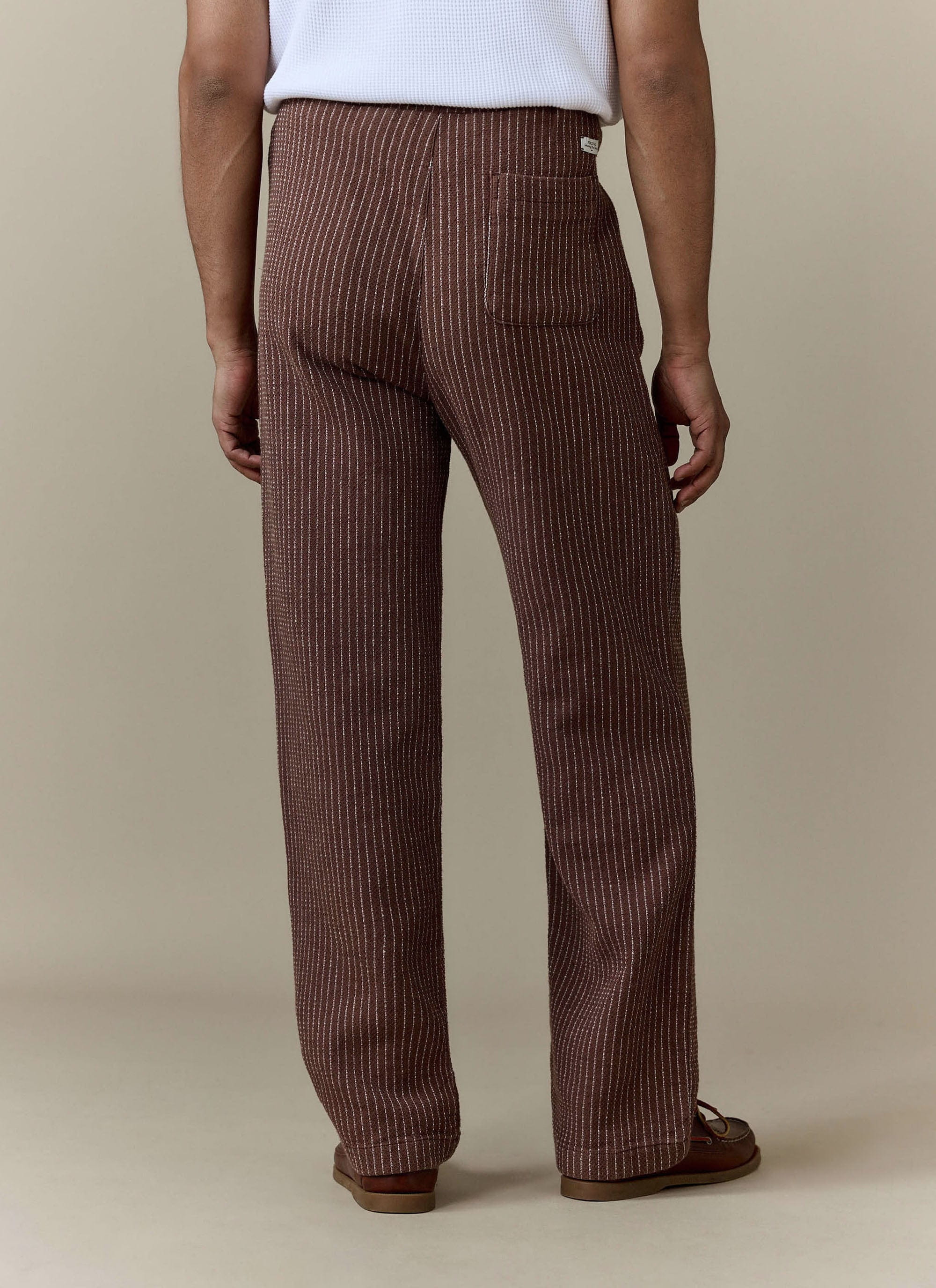 Back view of a model wearing the brown pinstripe Sorrento Wide Leg Trousers from Percival.