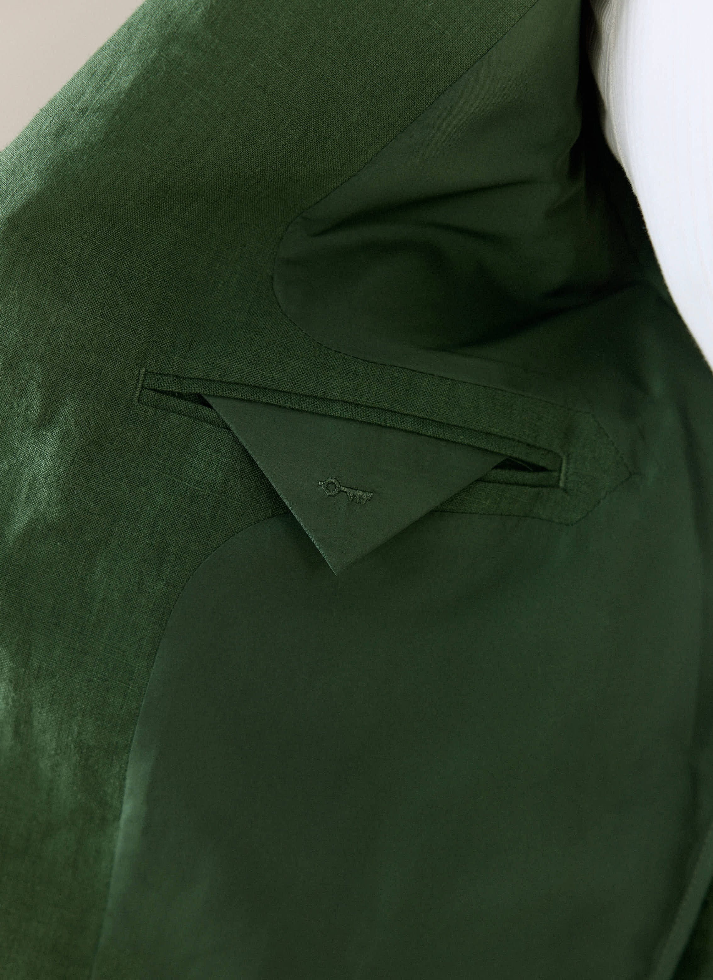 Internal pocket and lining detail of the Percival forest green linen blazer, featuring a tonal embroidered key logo.