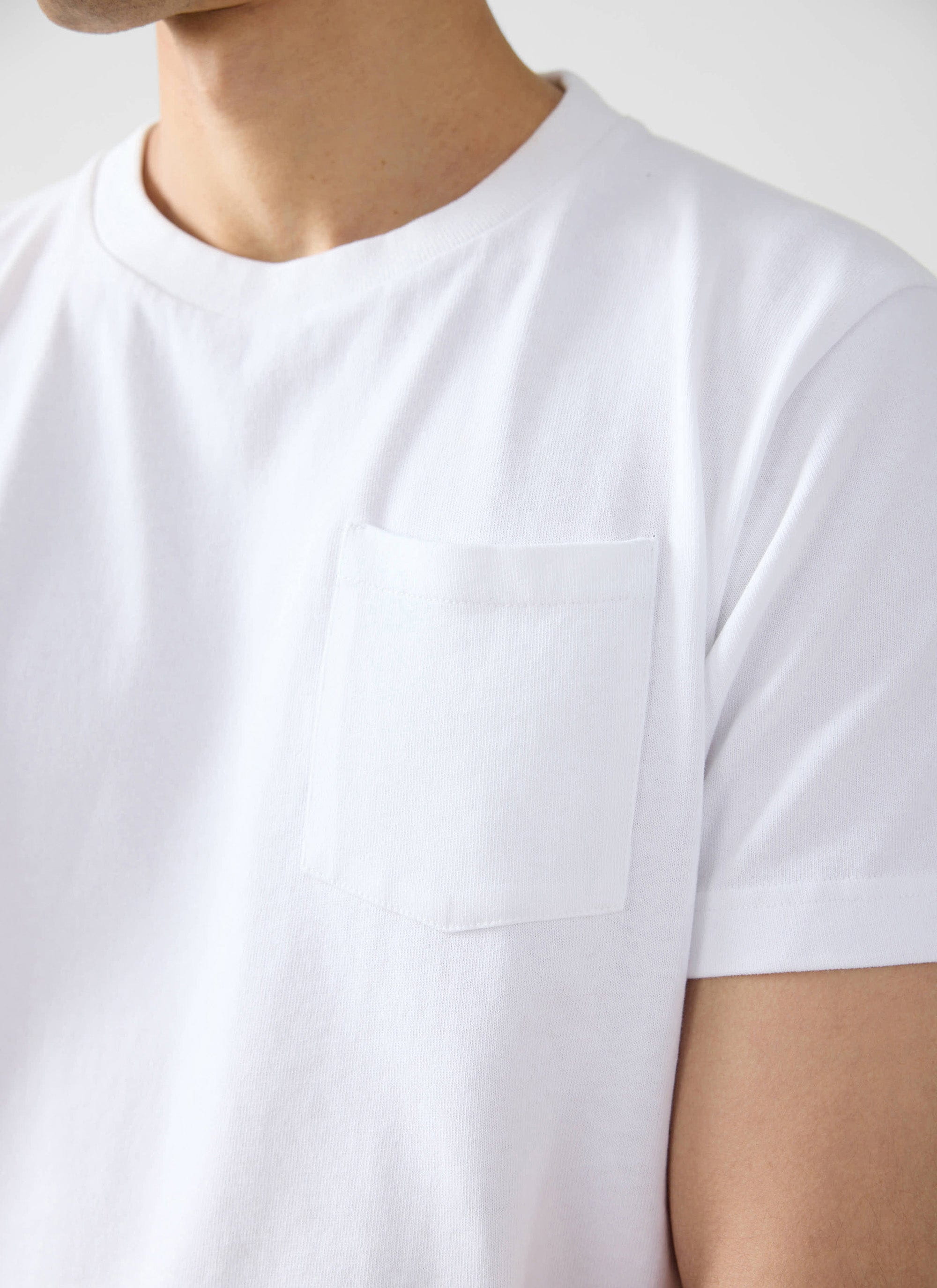 A close-up of the Percival Short Sleeve Pocket T Shirt in white, showing the organic cotton fabric and chest pocket detail.