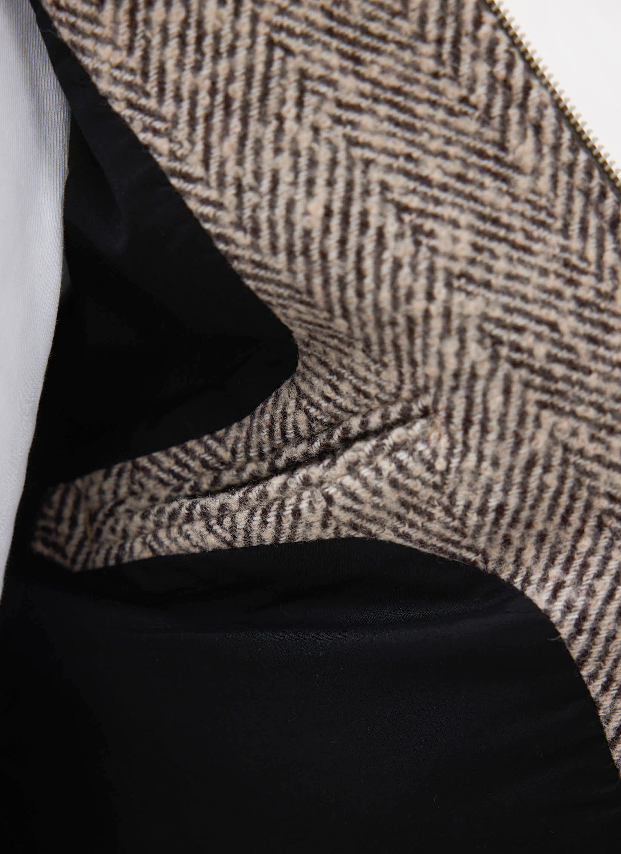 A detail shot of the Percival Herringbone Zip Jacket in ecru wool, highlighting the herringbone weave and black lining.