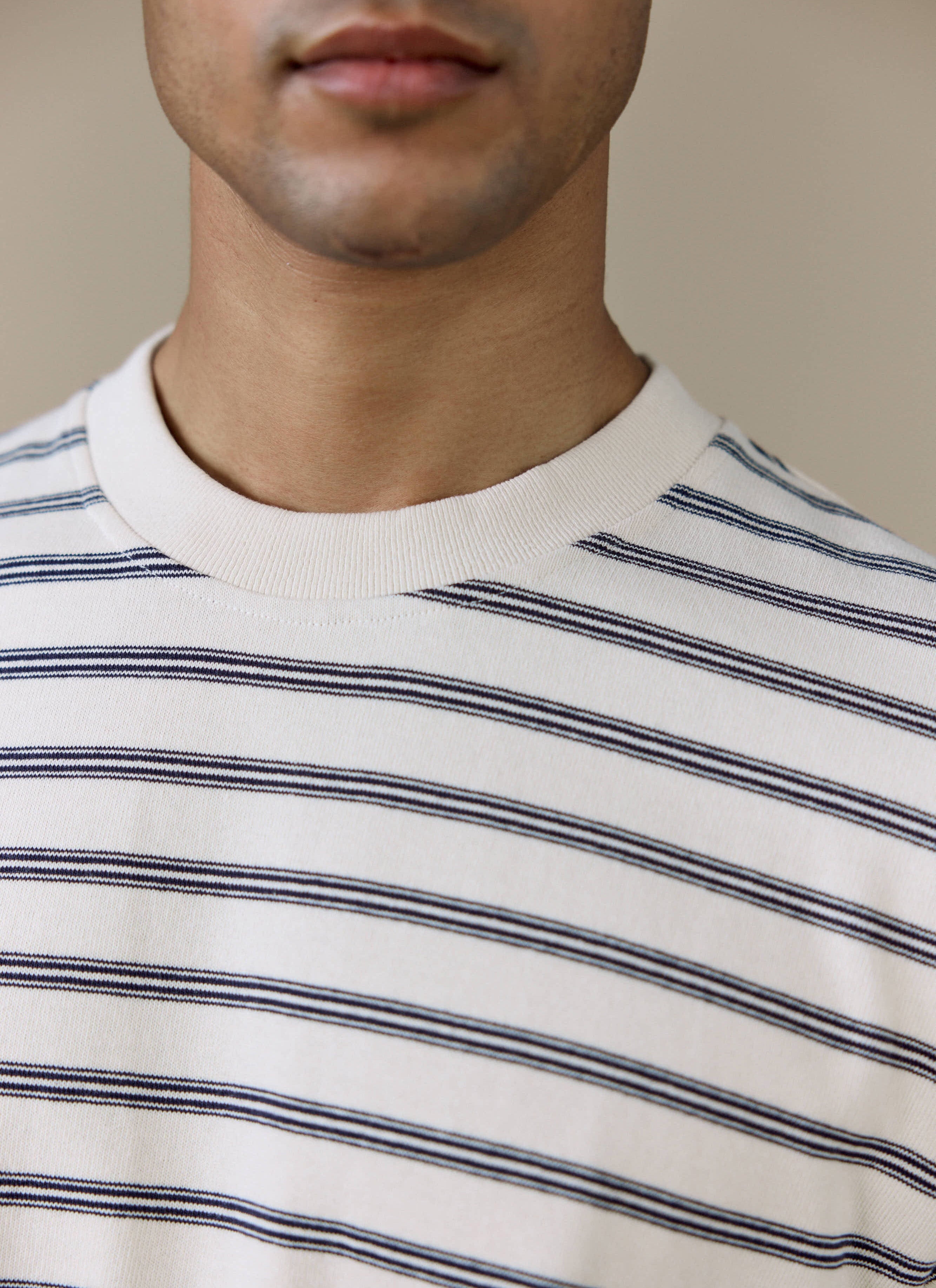 Close-up of a model wearing the Percival Arlo Raw Hem Breton T Shirt in white stripe, showing the ribbed crew neck.