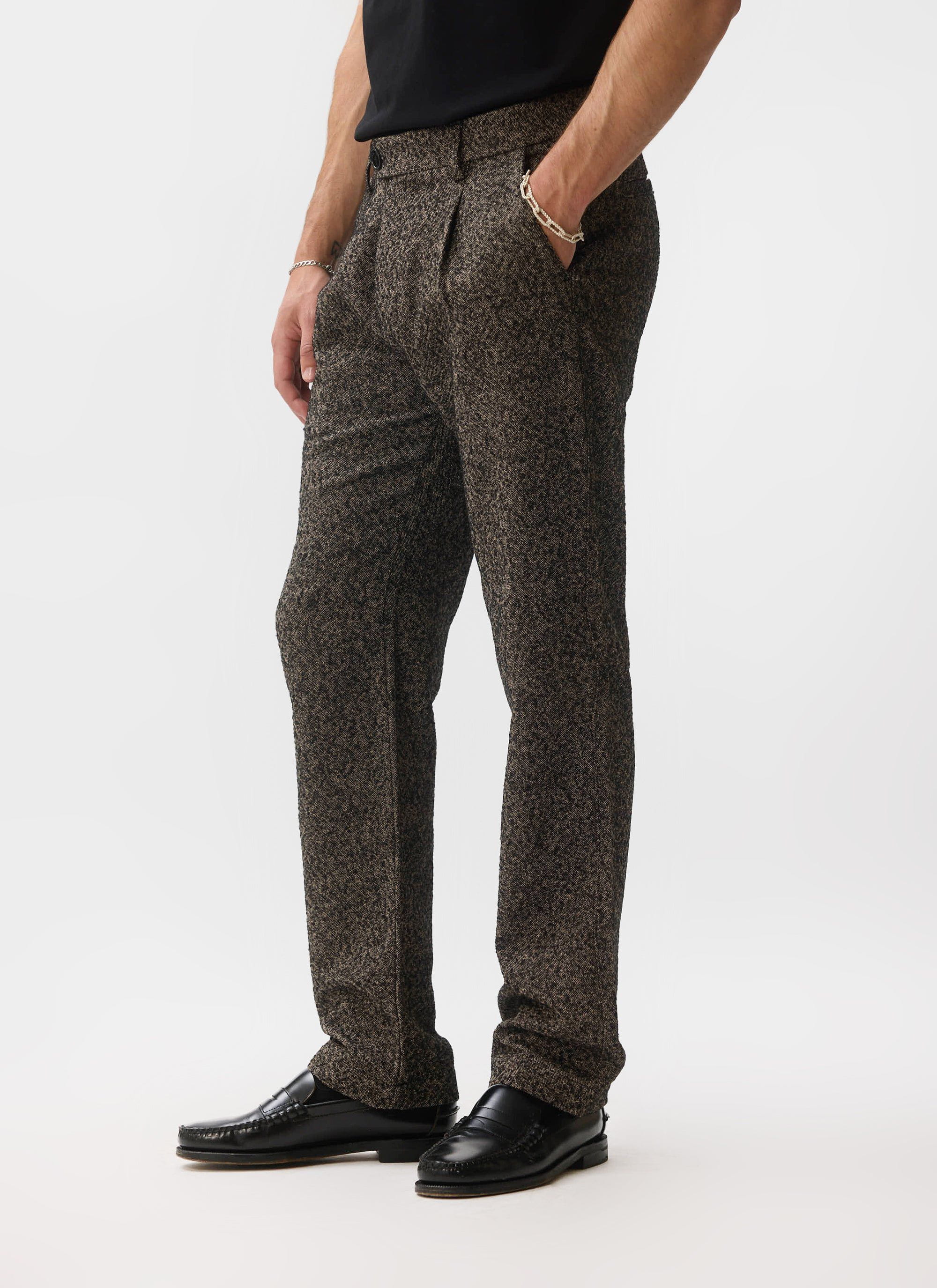 A model wears the Percival Blyton Trousers in a grey nep fabric, styled with a black t-shirt and black loafers.
