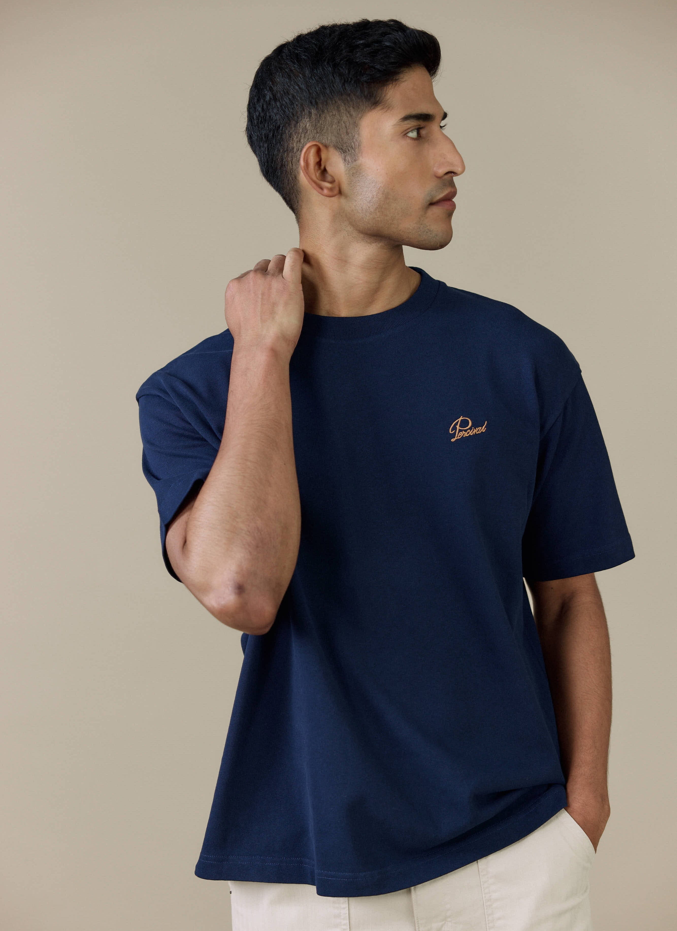A model wearing the navy Perci Script T Shirt from Percival, featuring contrast script embroidery on the chest.