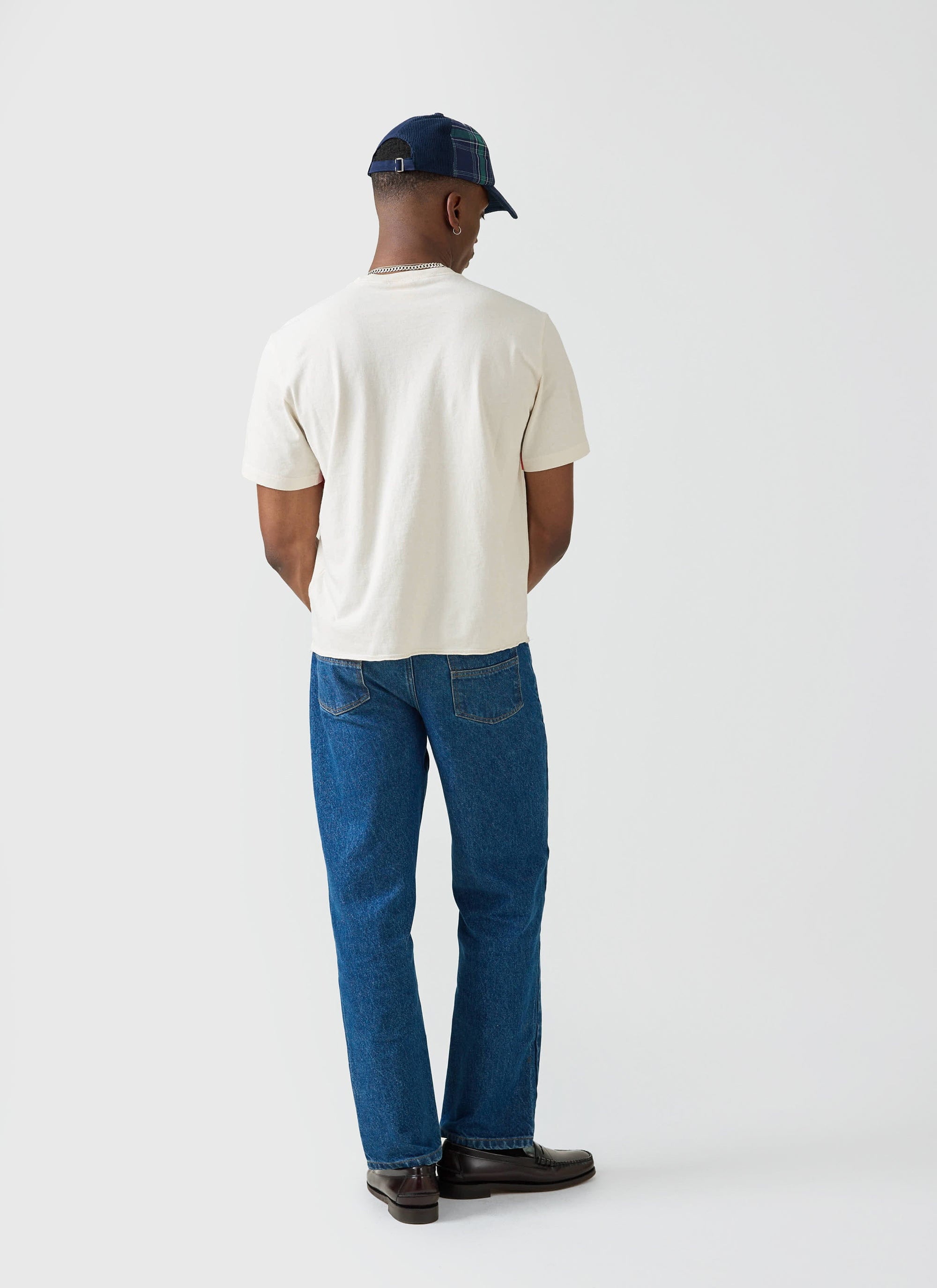 A model seen from behind wearing the Champion x Percival Flag Stripe Raw Hem T-shirt in ecru with blue jeans.