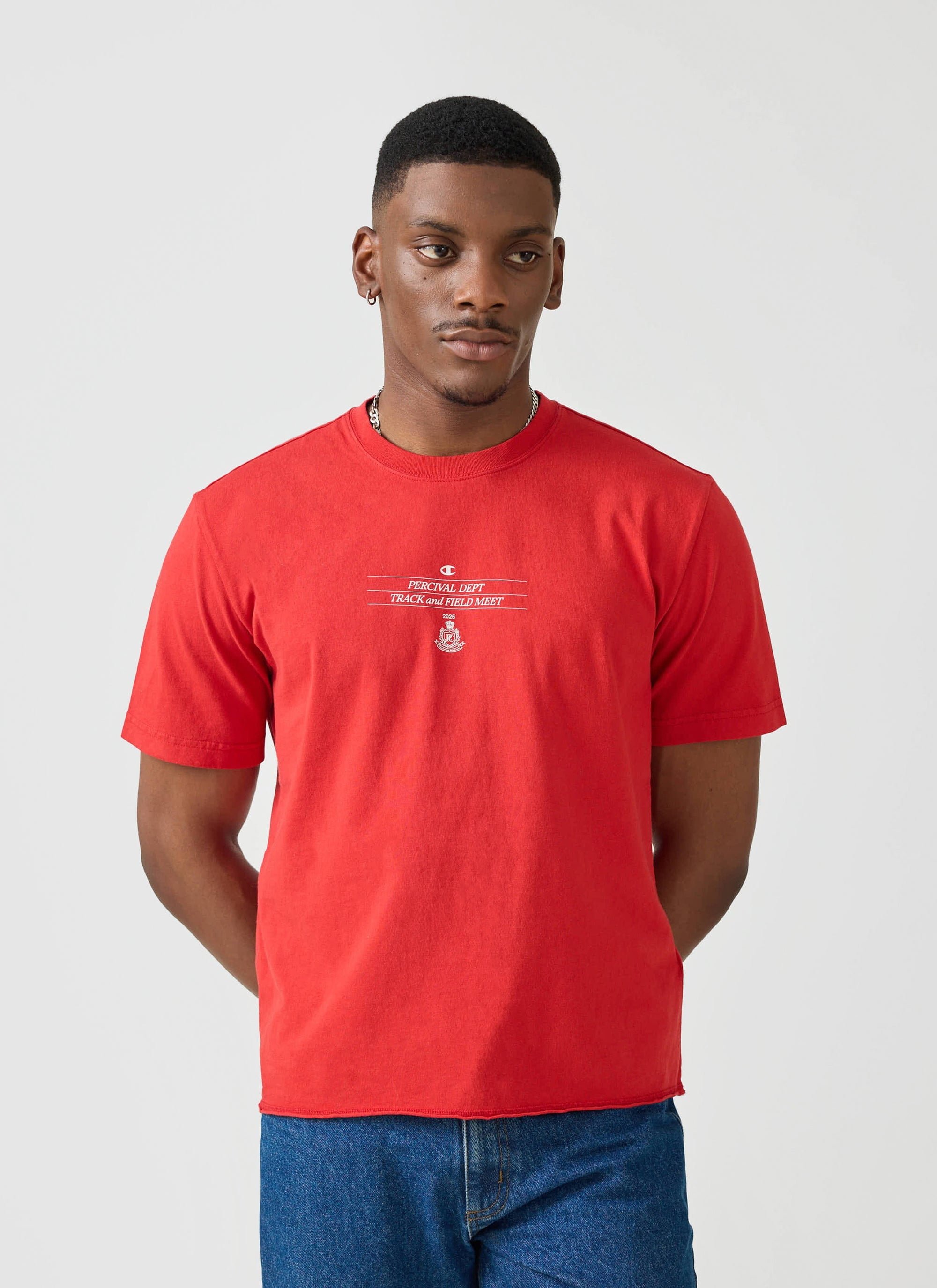 A model wears the red Champion x Percival Track and Field raw hem t-shirt against a clean studio background.