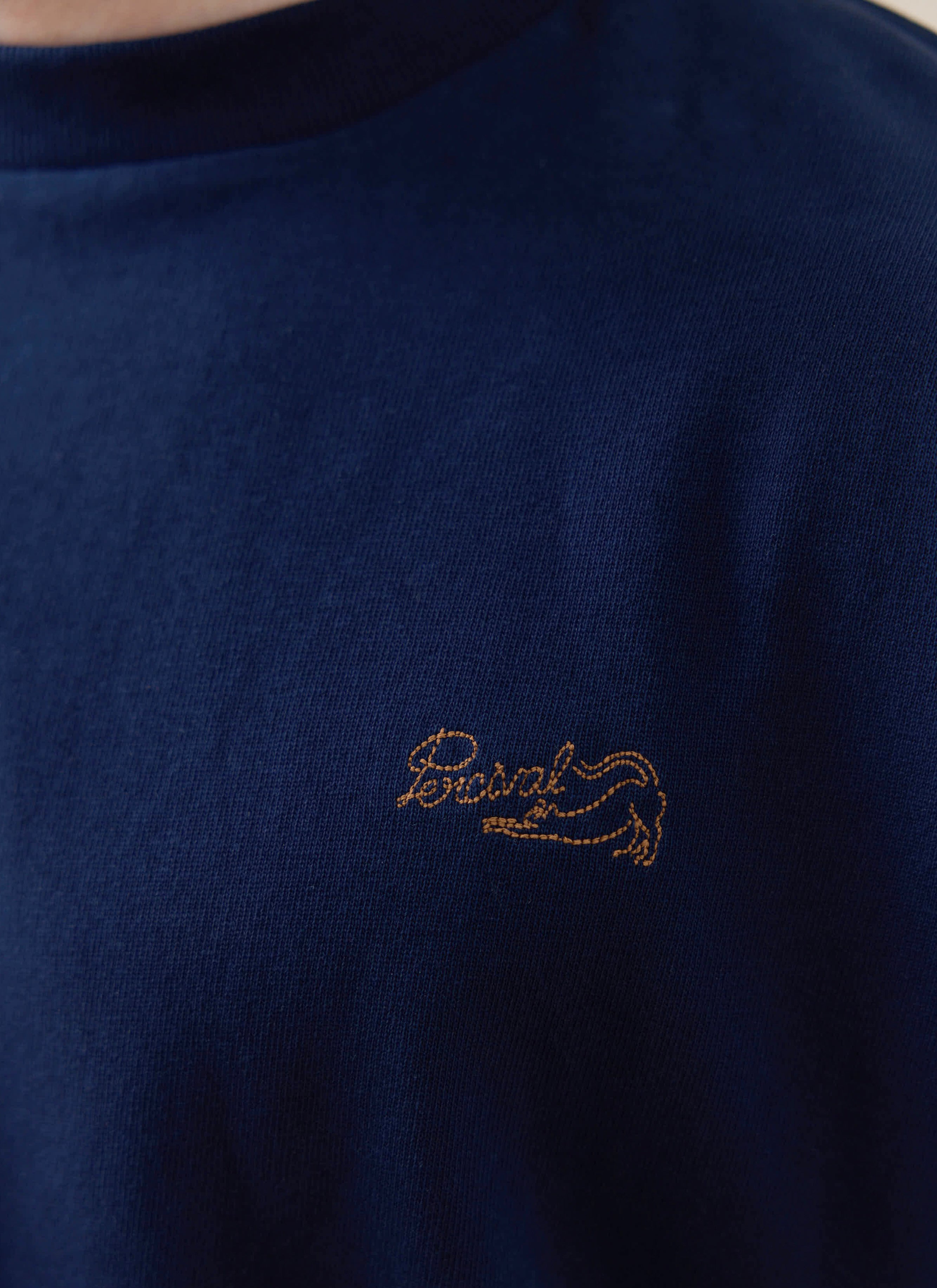 Gold-stitched Percival logo on the navy Clarke T-shirt, a piece from our organic cotton SS26 collection.