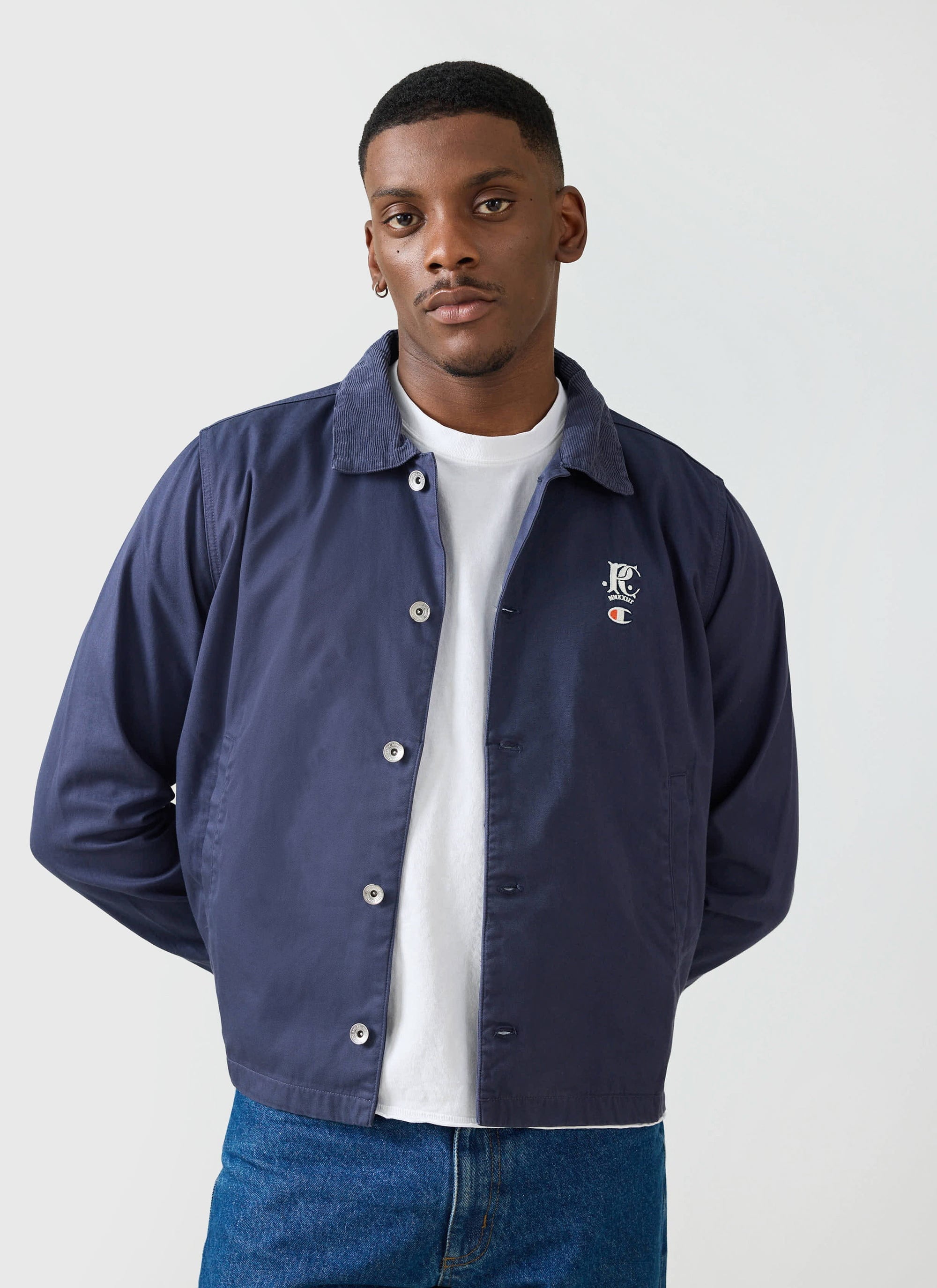 A man models the navy Cord Collar Jacket from the Champion x Percival collection, worn over a white t-shirt.
