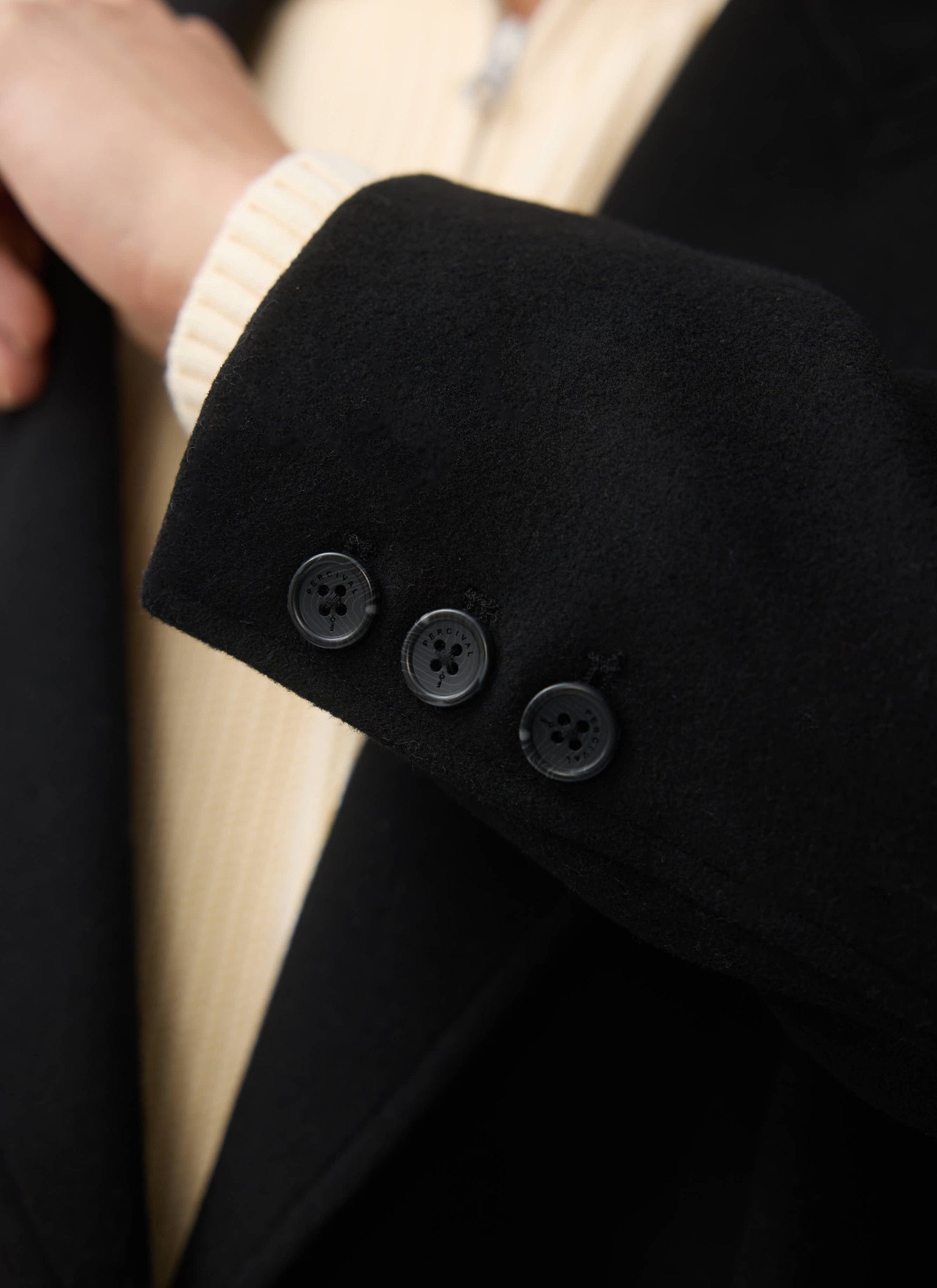Close-up detail of the branded buttons on the cuff of the Percival Double Breasted Overcoat in black wool.