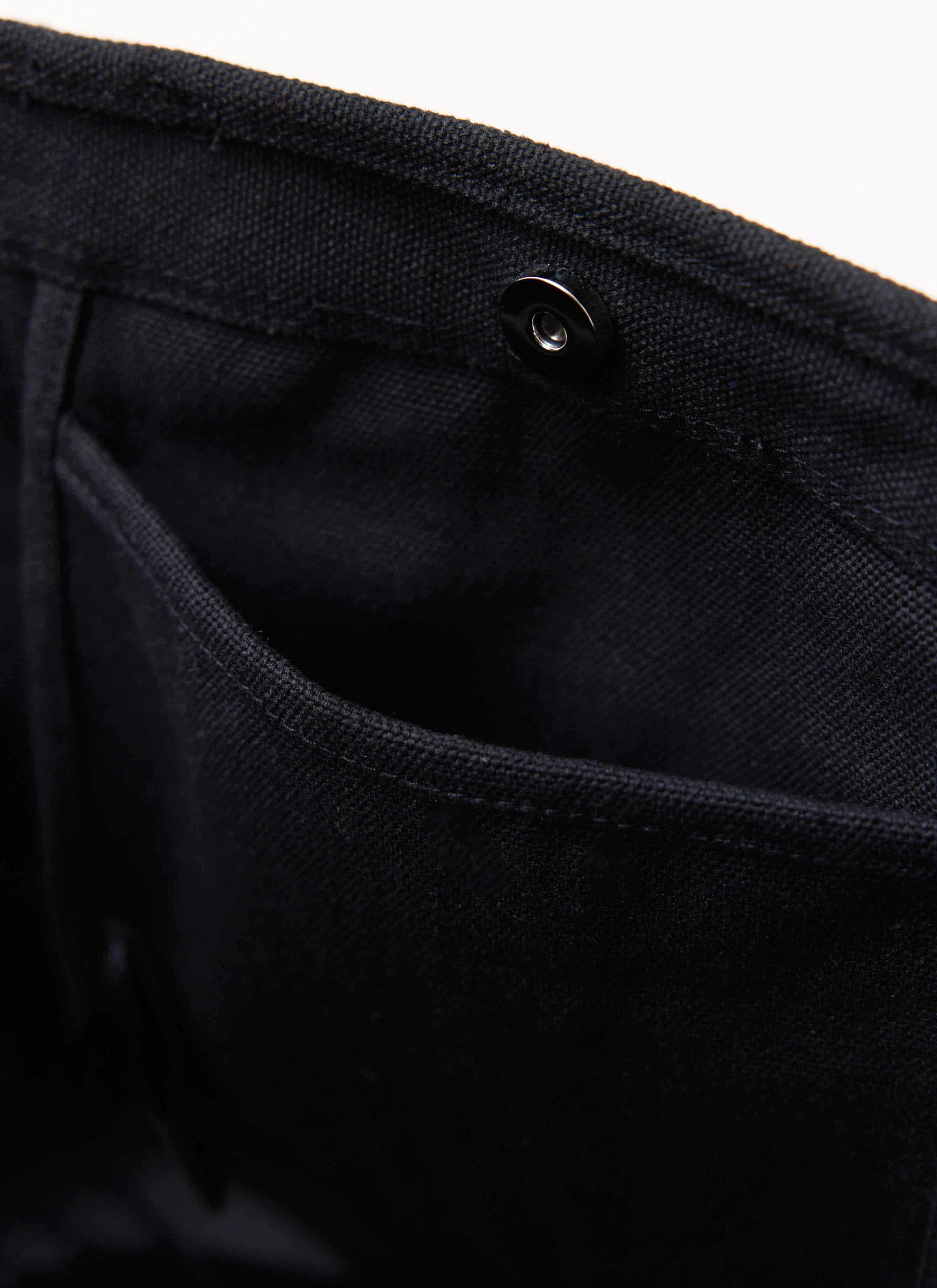 A close-up of the internal pocket and magnetic snap closure on the black canvas tote bag by Percival.