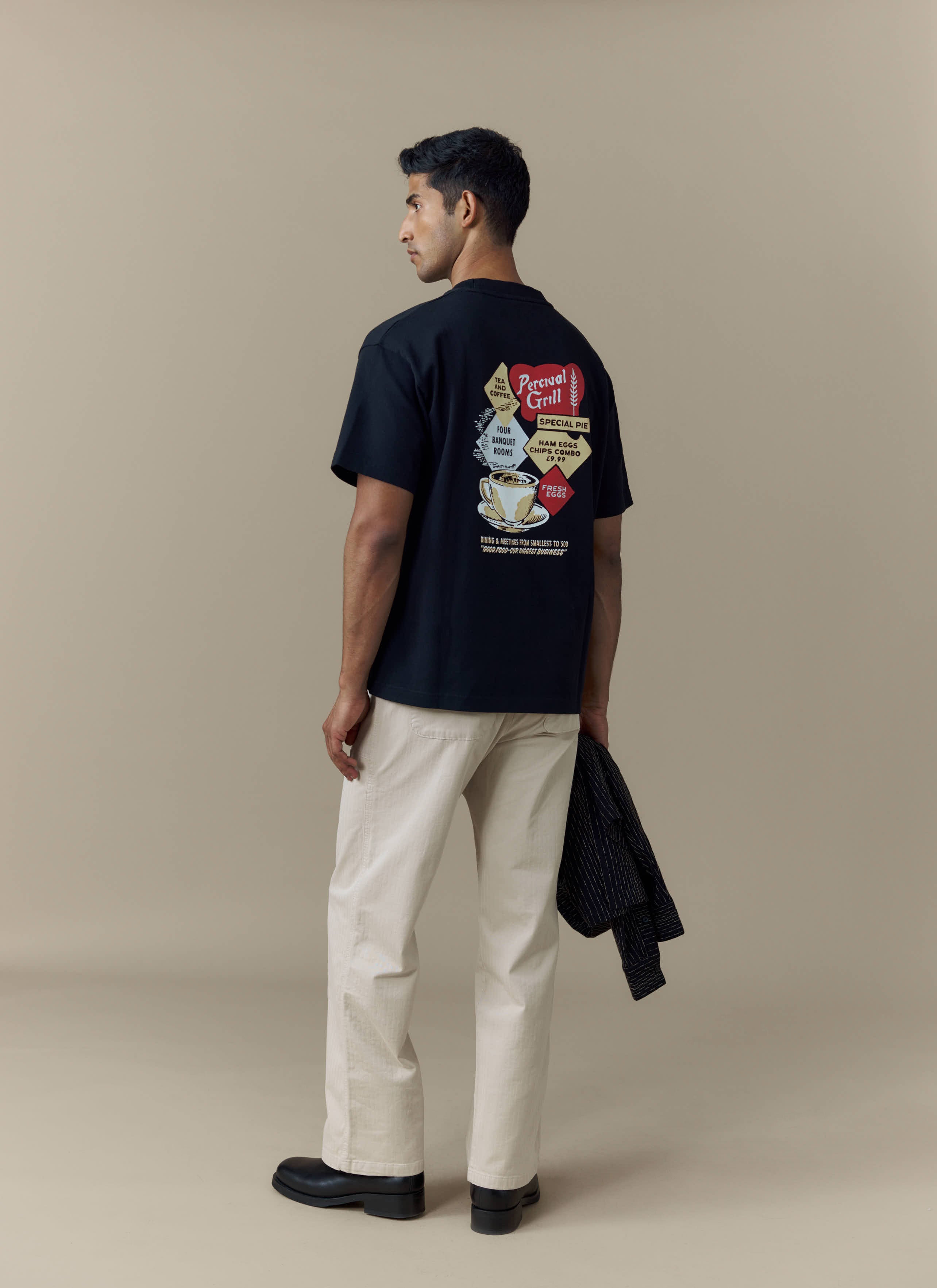 A model wears the black Percival Grill Oversized T-Shirt, showing the colourful vintage diner-style graphic on the back.