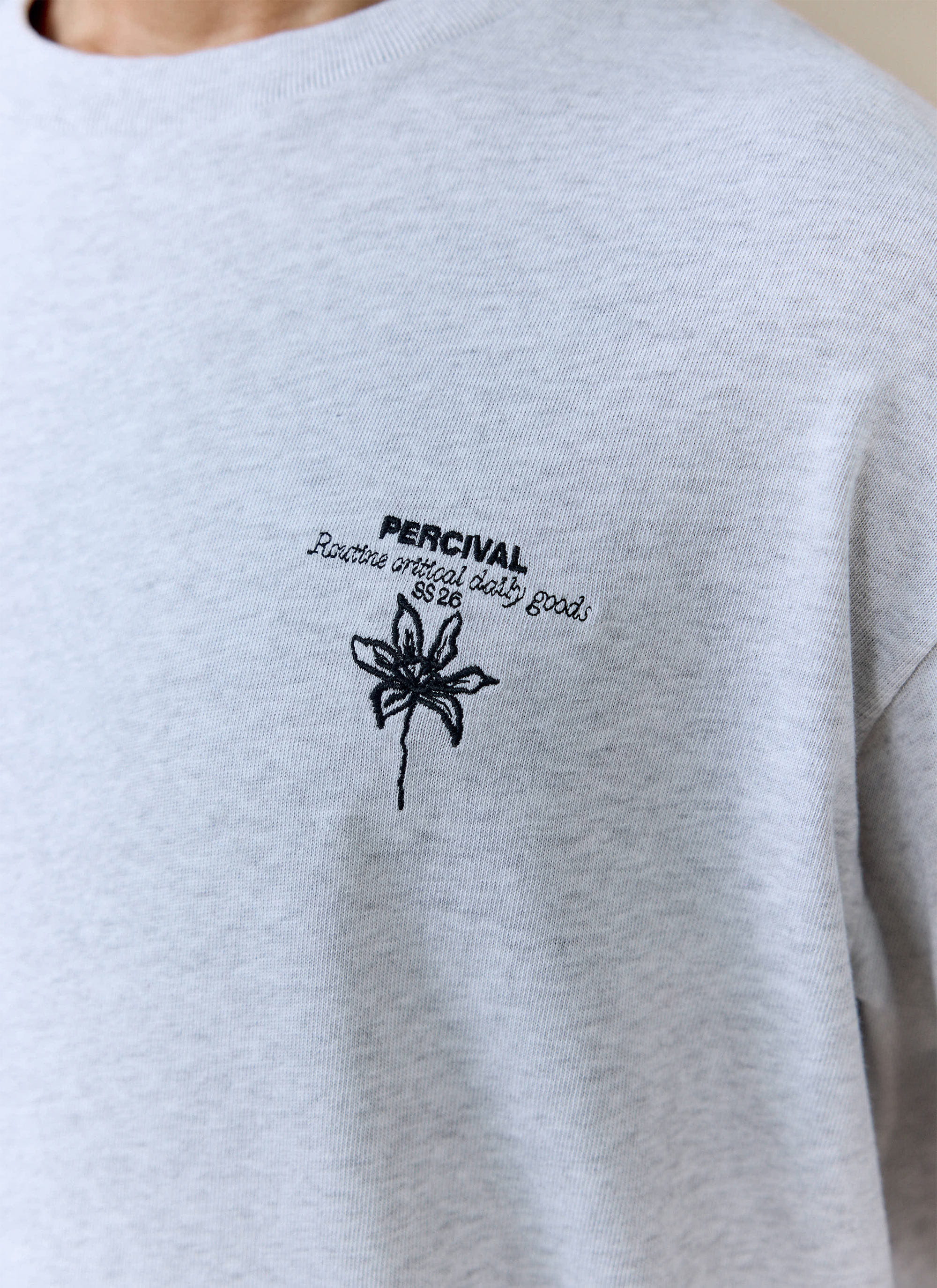 A close-up of the black chest embroidery on the grey organic cotton Percival Melvin Oversized T Shirt.