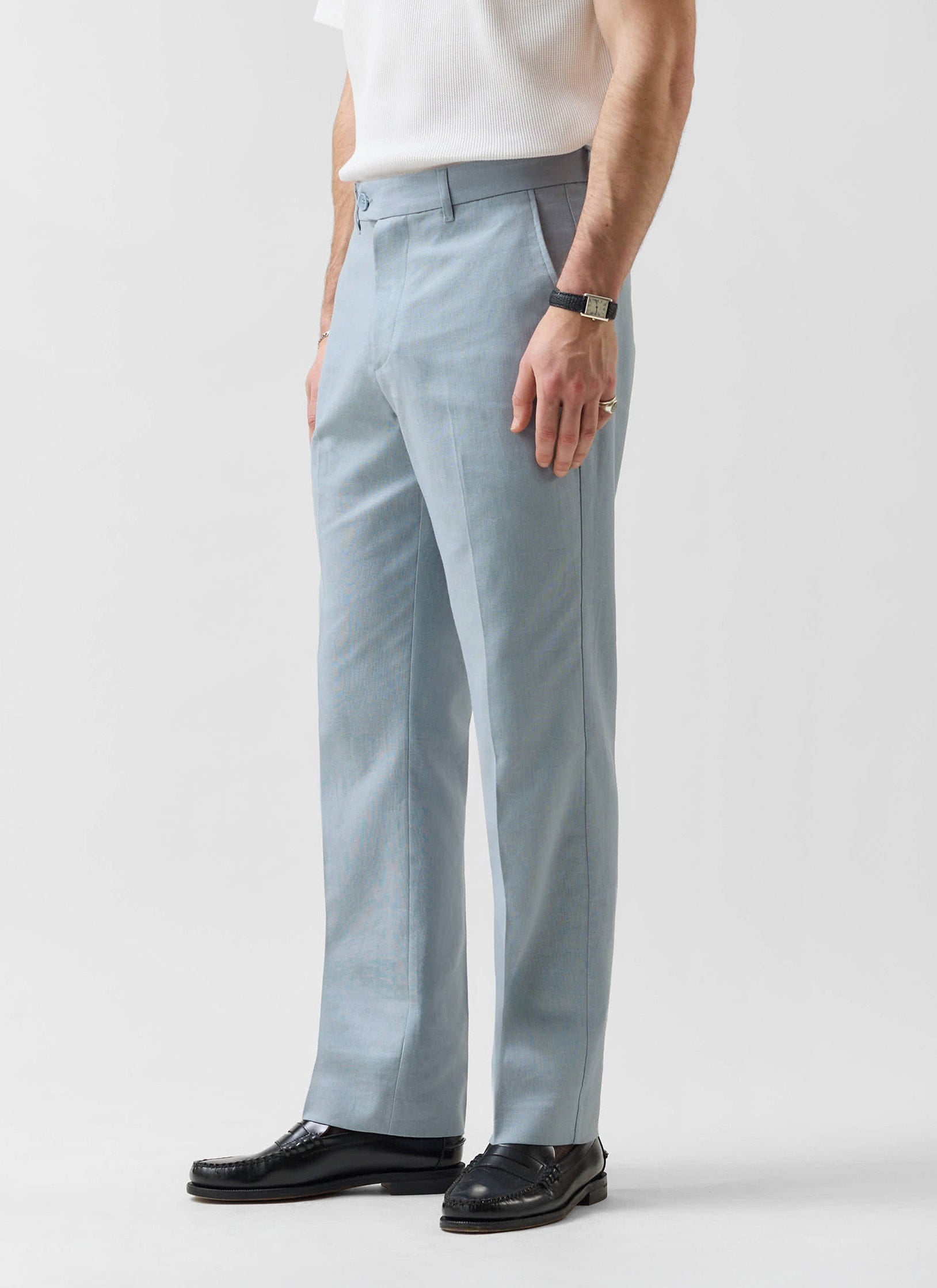 A model wears the Percival Tailored Linen Trousers in light blue with a white t-shirt and black loafers.