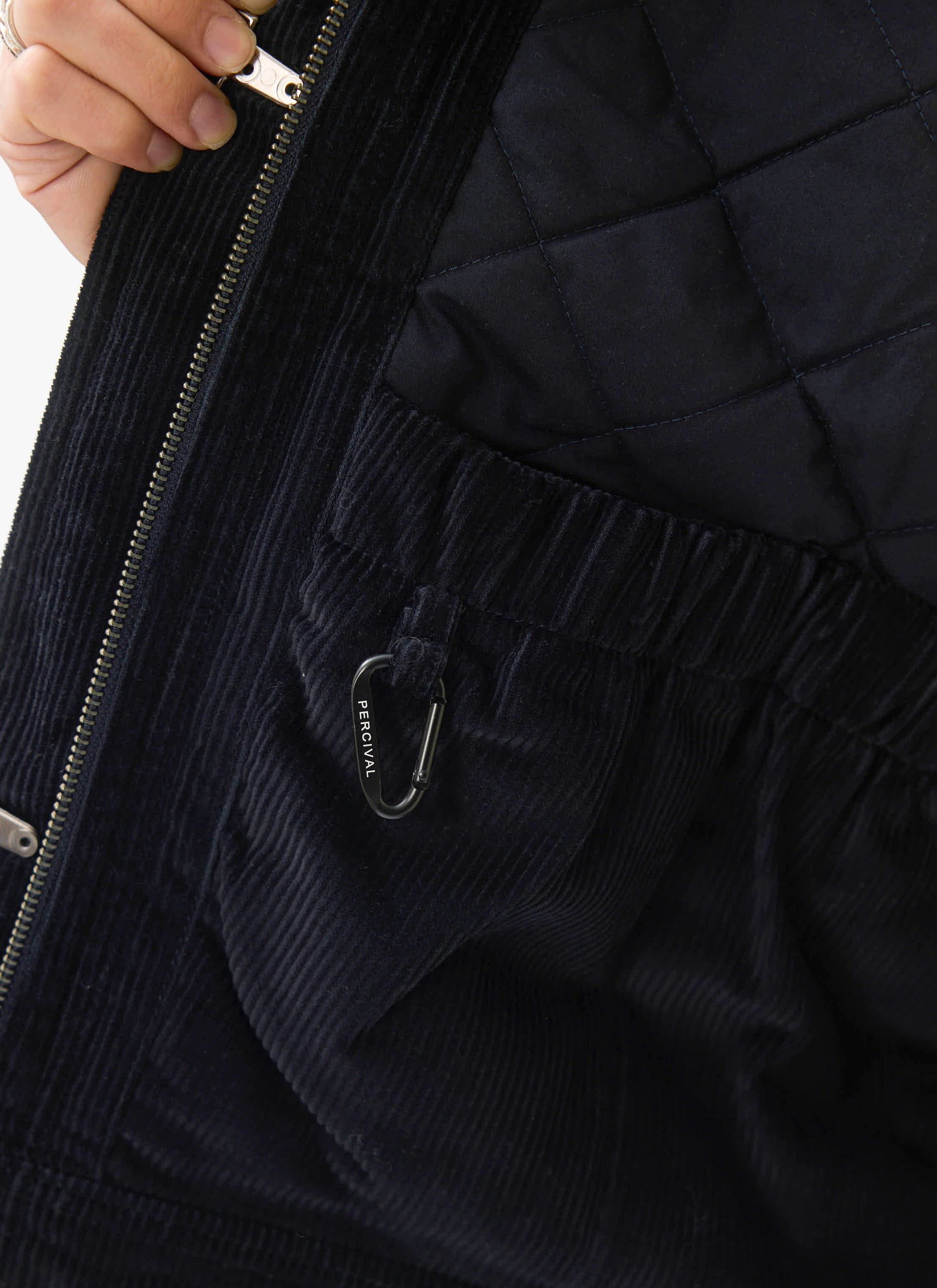 A close-up of the inside of the Percival Fontane Wax Jacket in navy, showing the quilted lining and branded carabiner clip.