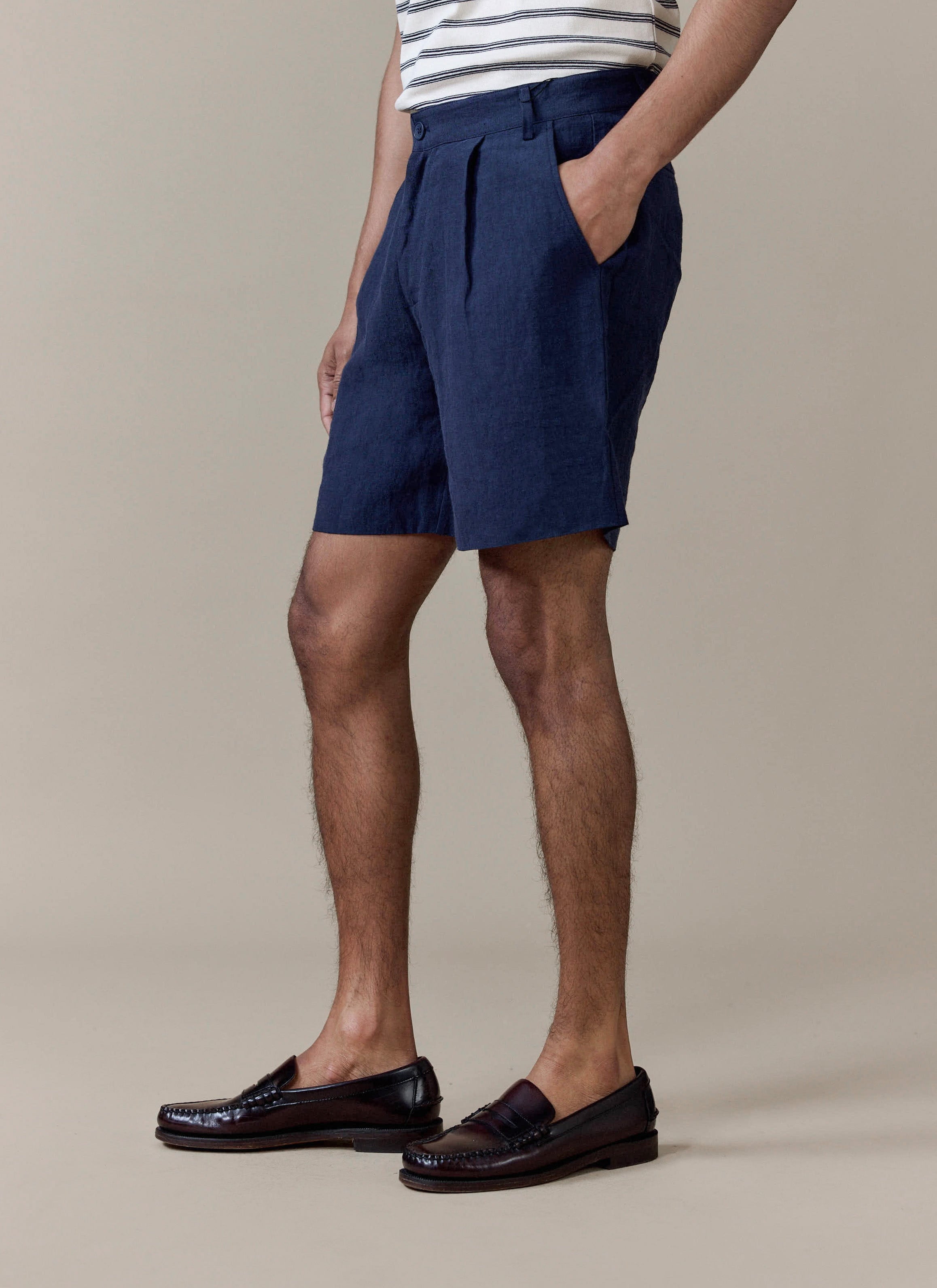 Navy pleated linen shorts from Percival, styled on a model with a striped t-shirt and dark leather loafers.