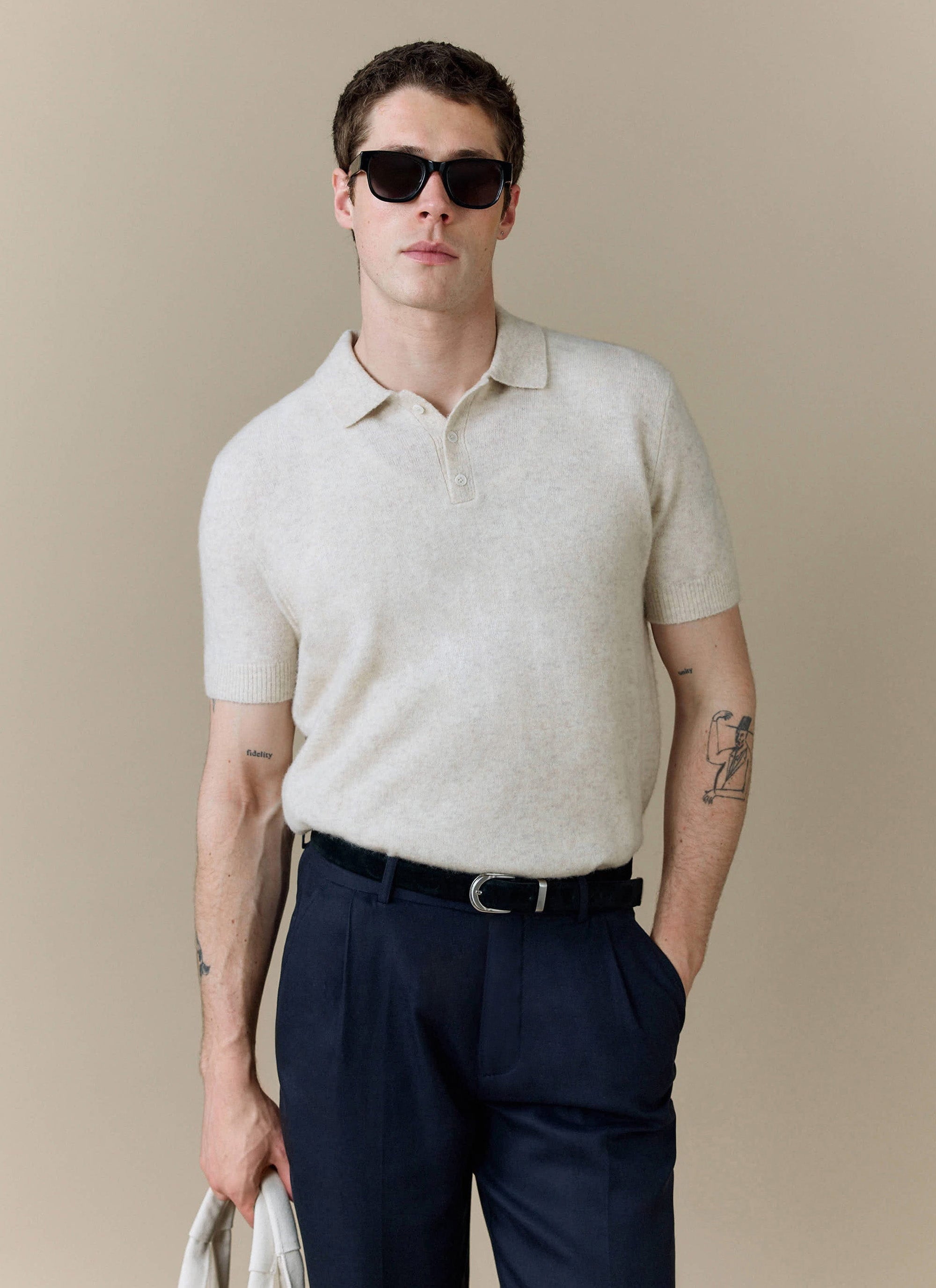 A model wears the Percival Collins Boxy Knitted Polo in ecru yak-wool, styled with dark trousers and sunglasses.