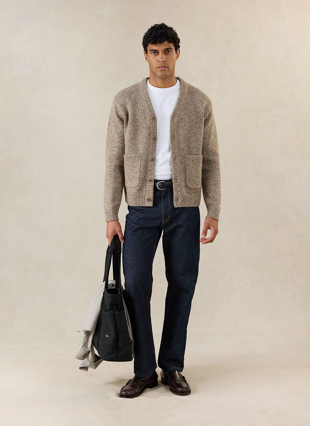 A model wears the Percival Rhodes White Glove Cardigan in oak cotton, styled with dark jeans and a black tote bag.