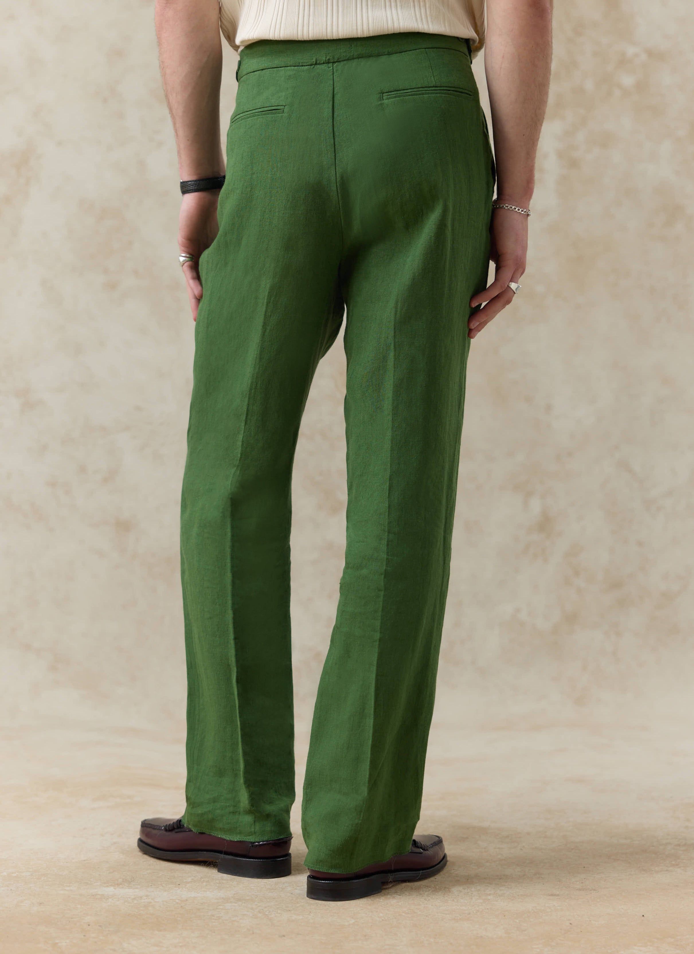 Rear view of the forest green linen pleated tailored trousers by Percival, showing the welt pockets and relaxed fit.