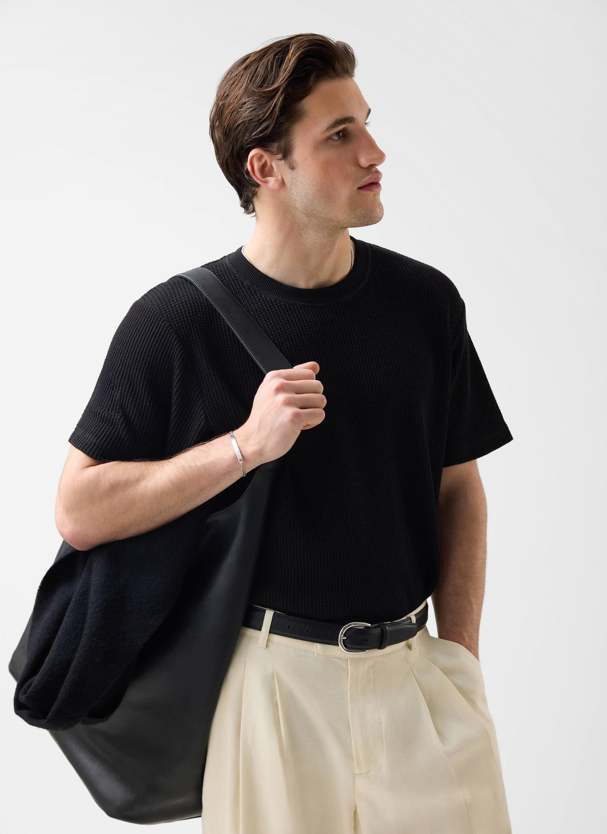 A model wears the Percival black Waffle Short Sleeve T-Shirt, styled with cream pleated trousers and a black tote bag.