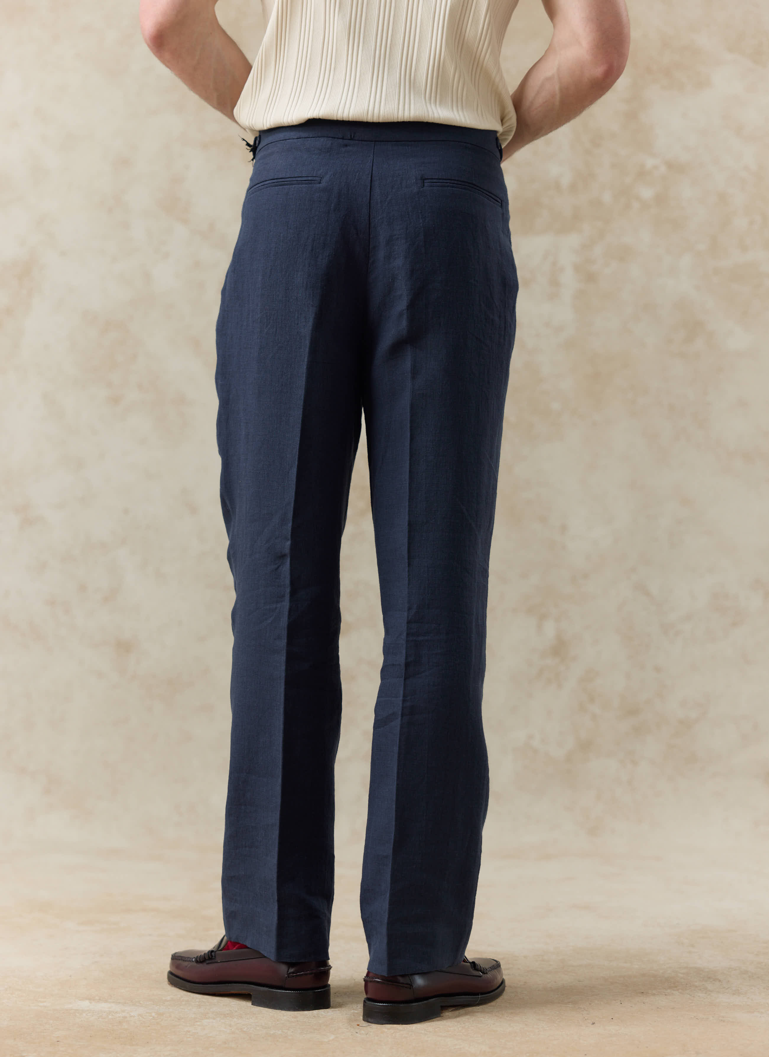 Rear view of Percival navy blue pleated linen trousers, showing the relaxed tailored fit and back welt pockets.