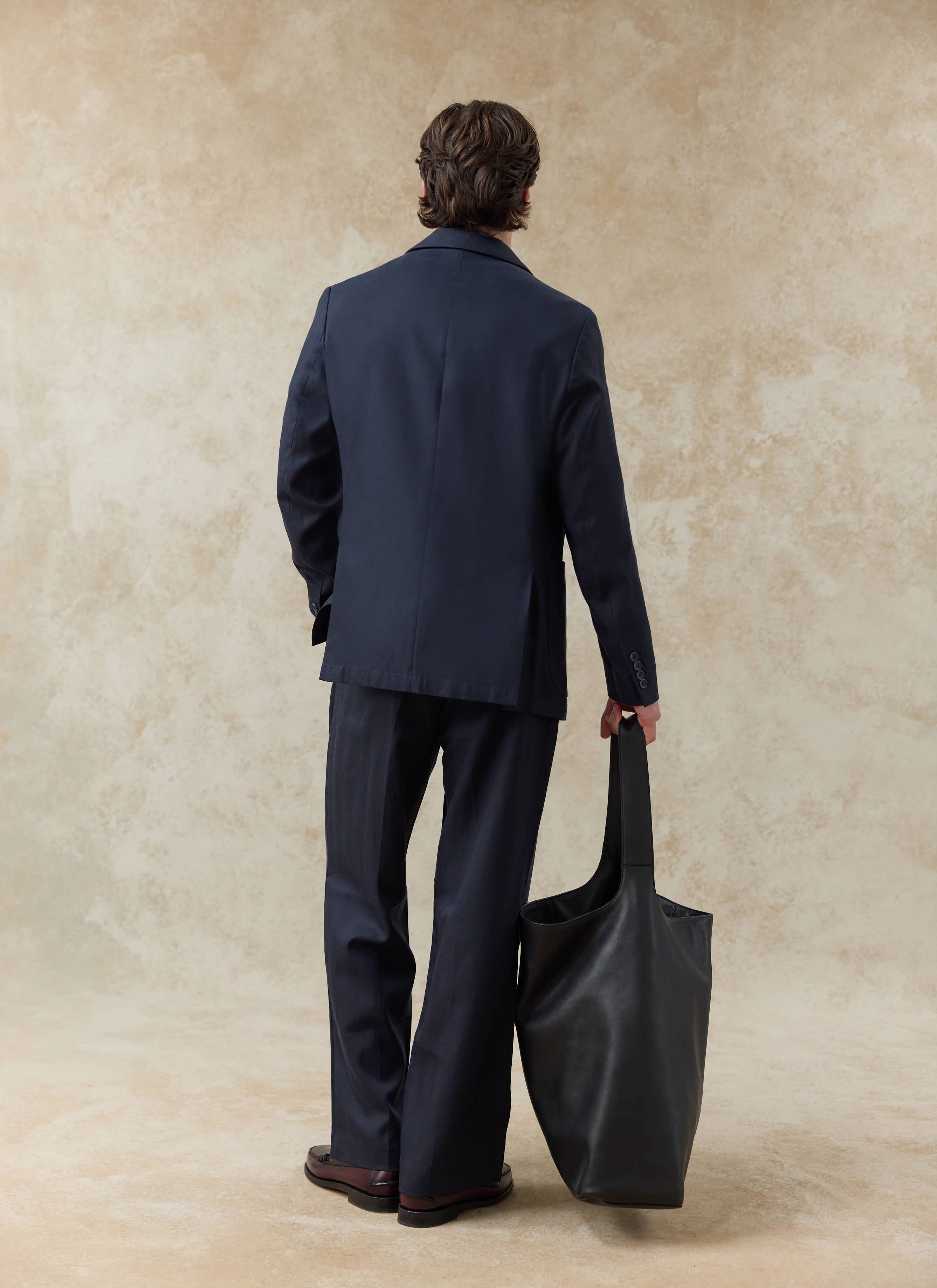 Rear view of the navy blue Percival Lyocell regular blazer, styled with matching trousers and a large black leather bag.