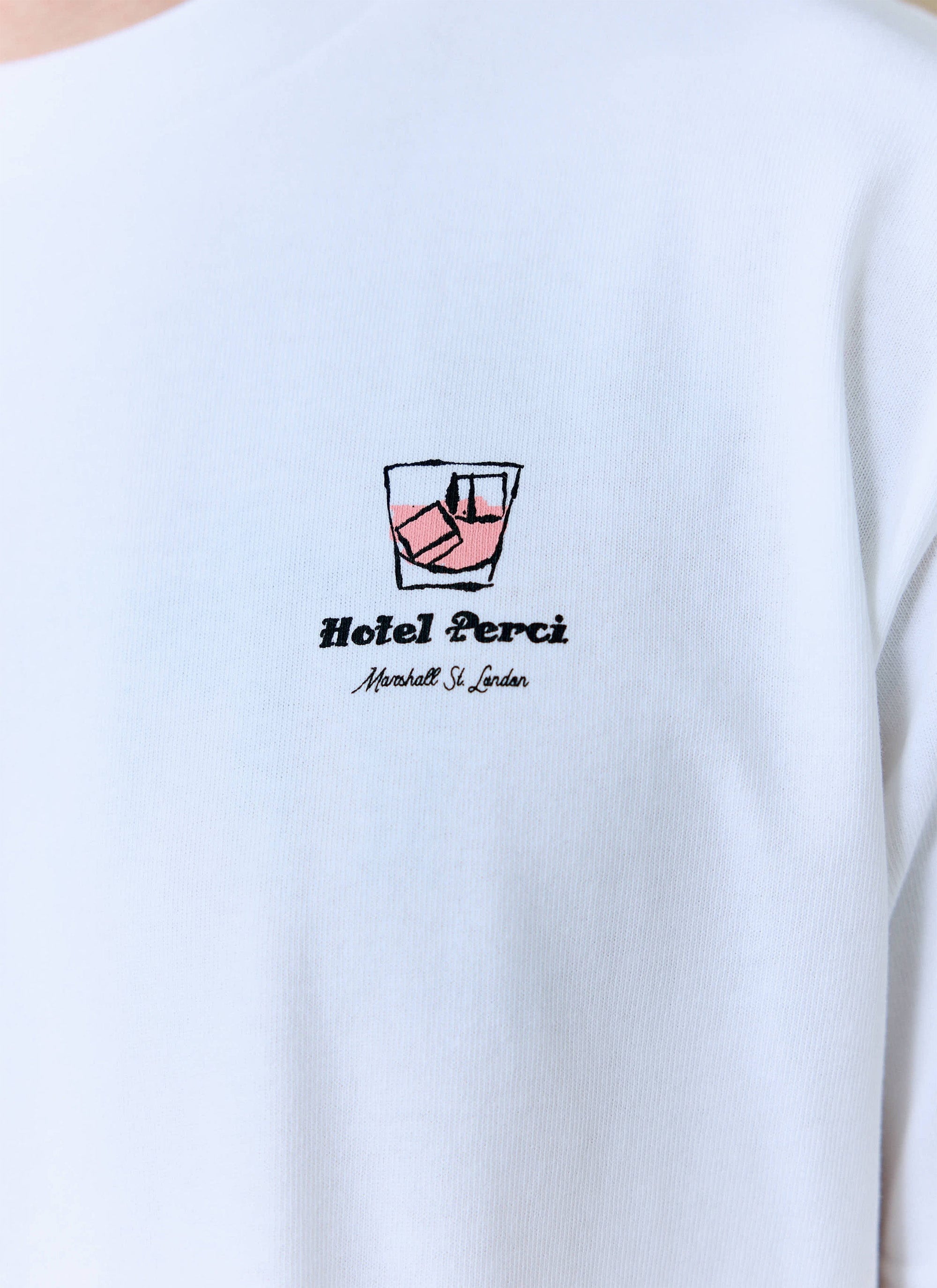 A close-up of the Hotel Bistro T-shirt from Percival, showing the embroidered cocktail graphic and 'Hotel Perci' text.
