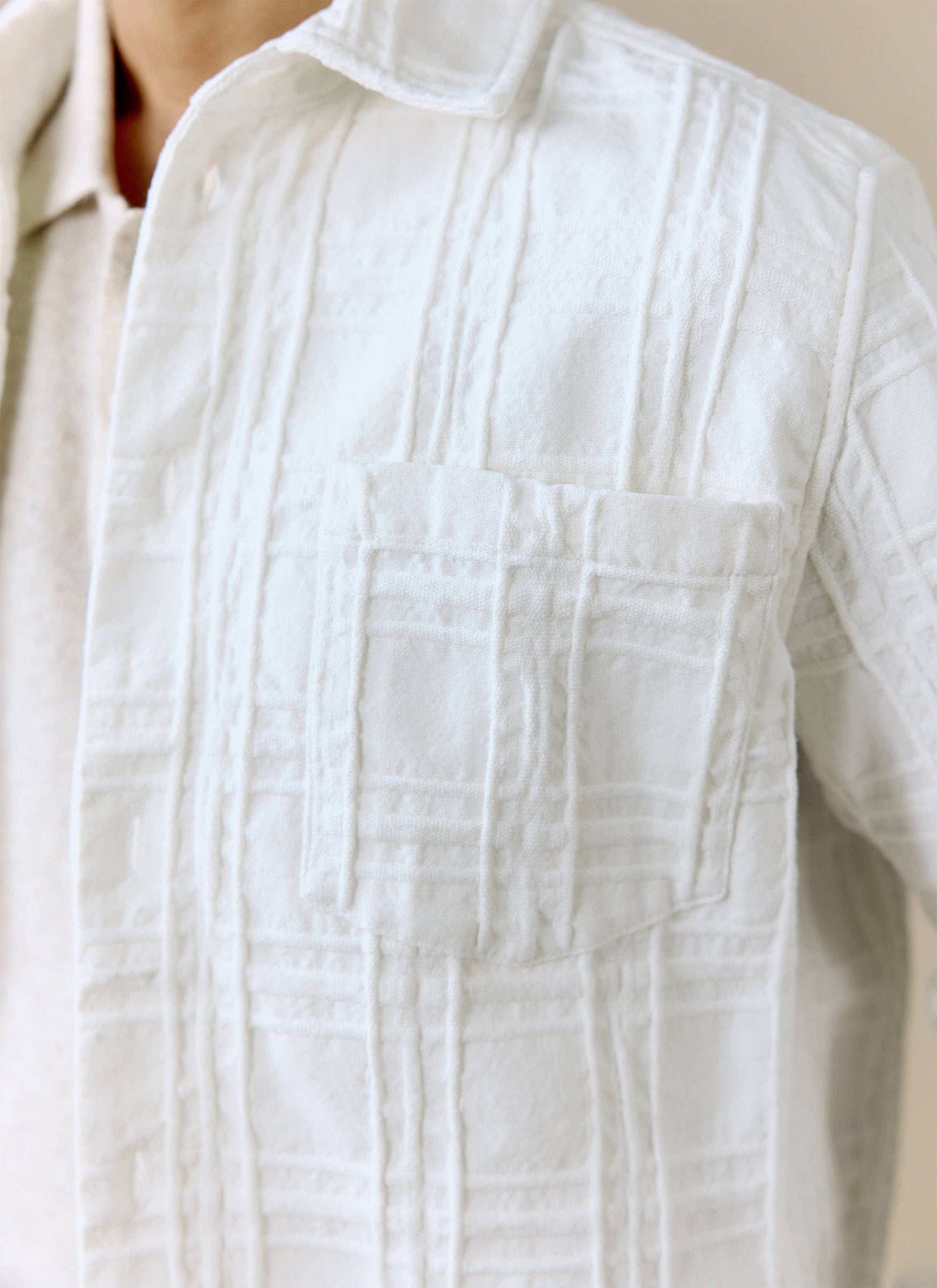 A close-up shot showing the textured woven fabric and chest pocket of the Percival Canyon Heavyweight Overshirt in ecru.