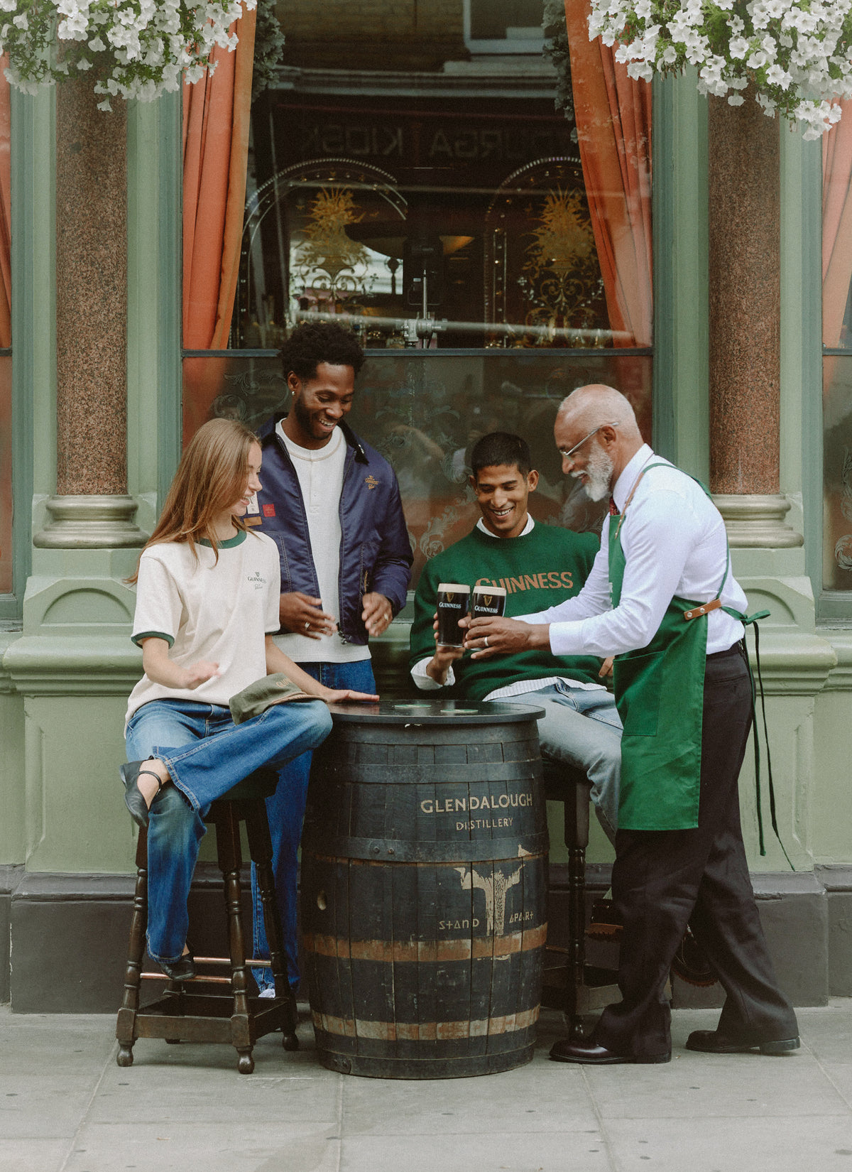Models and a bartender enjoying pints of Guinness outside a traditional pub during the Guinness x Percival collection shoot.