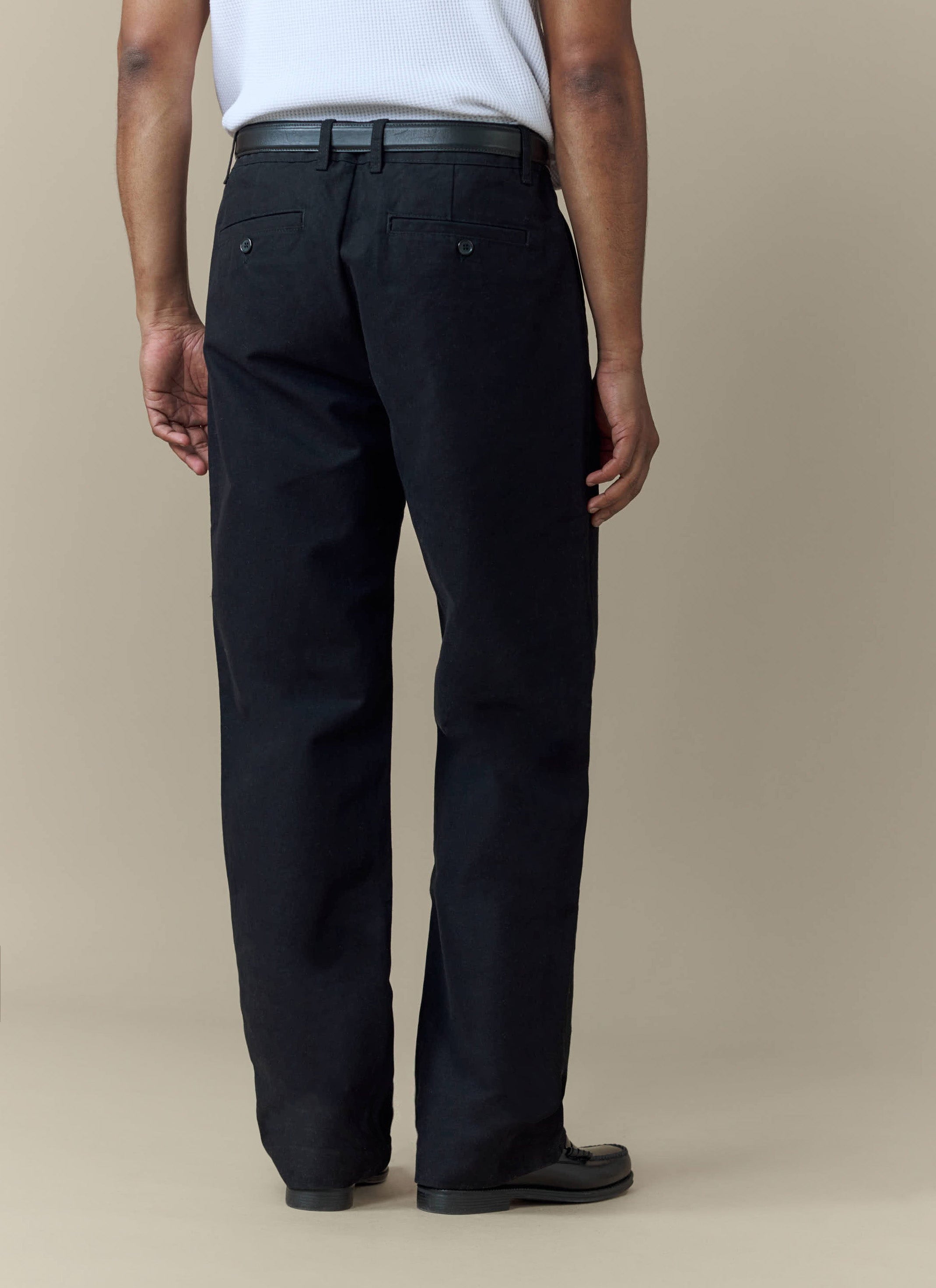 The back view of a model wearing the black Seb Inverted Pleat Trousers by Percival.