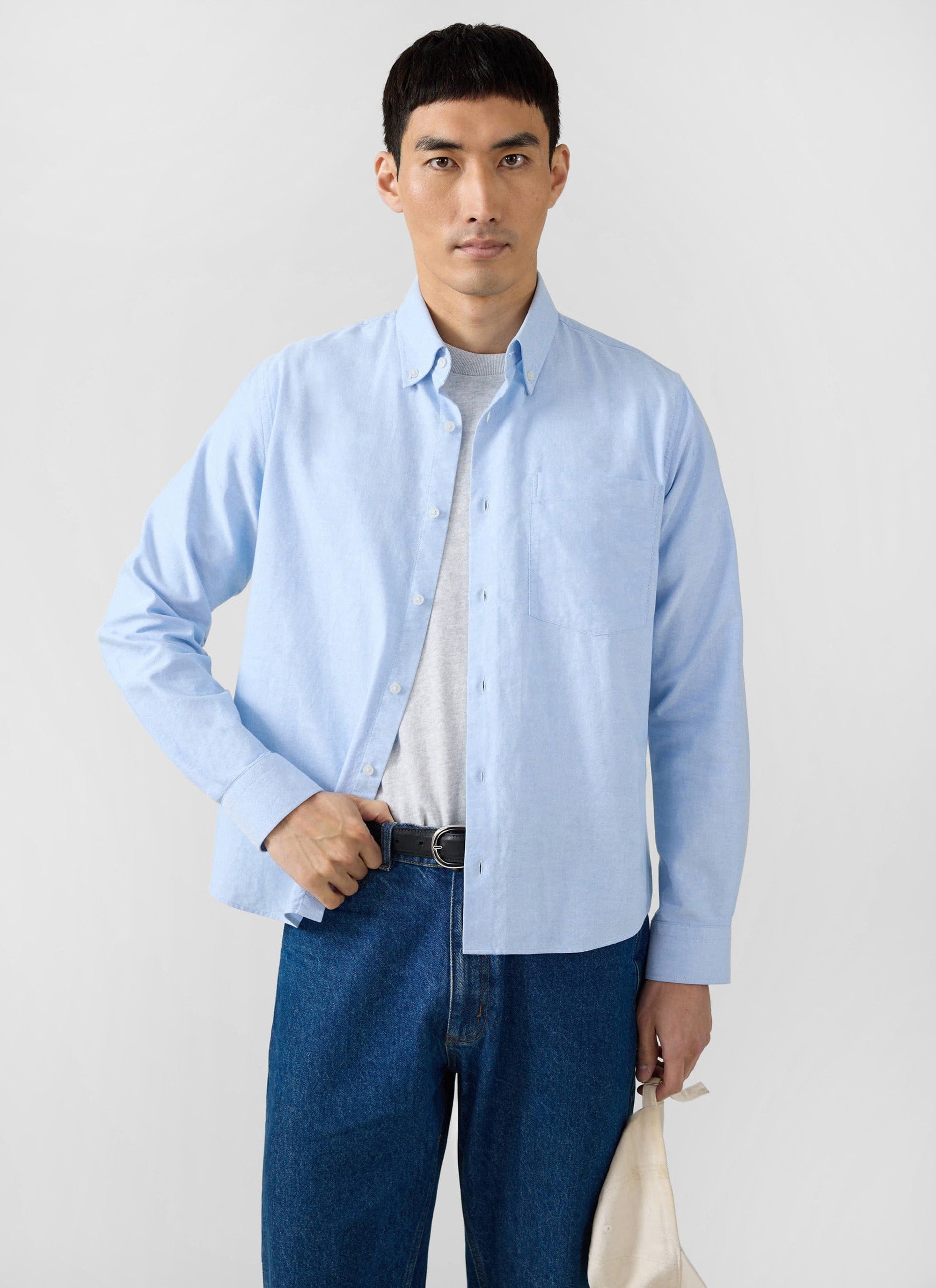 A man models the light blue Percival Oxford shirt, worn open over a t-shirt with dark blue jeans.