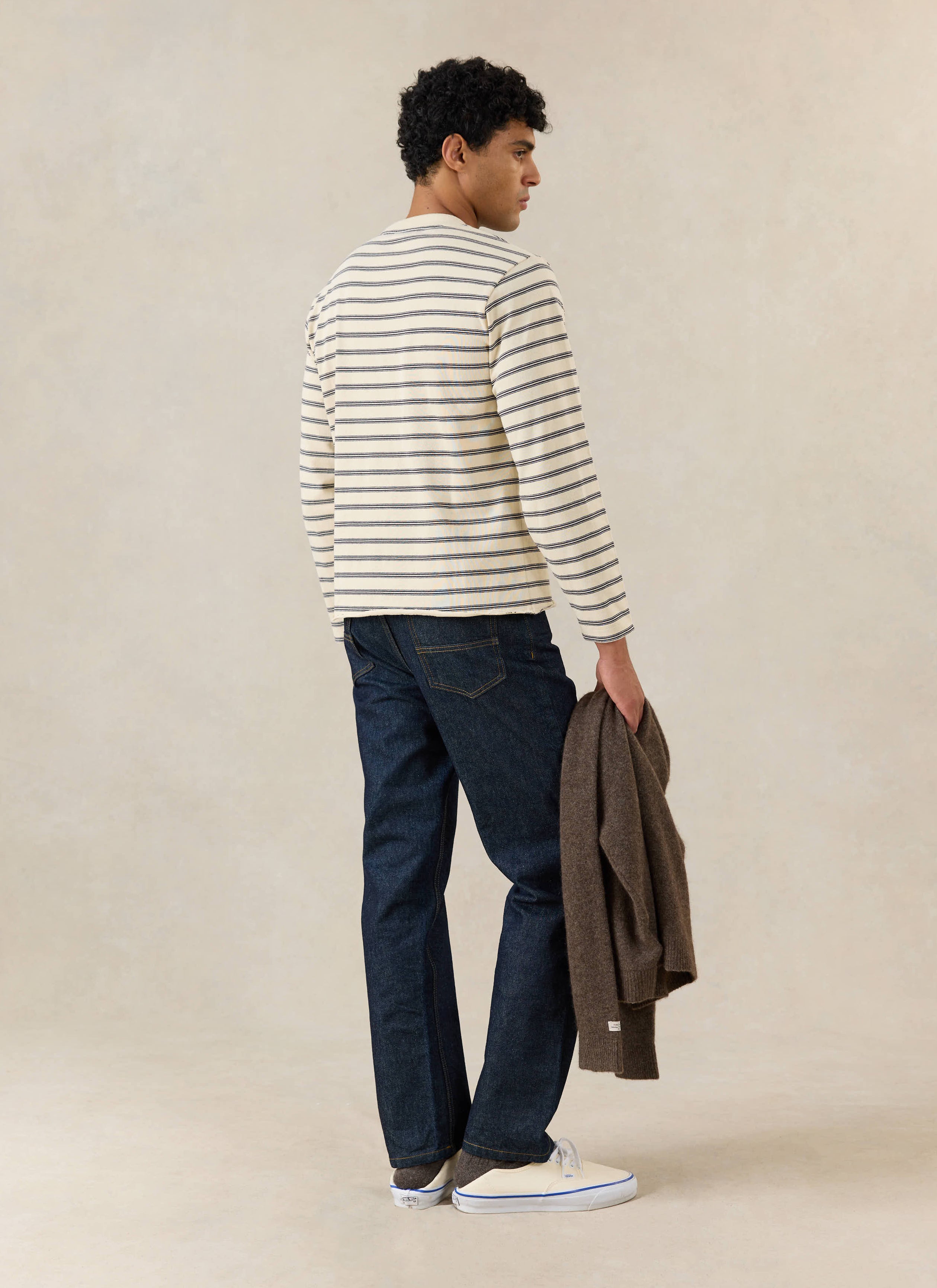 A model wears the Percival Arlo white stripe Breton long sleeve T-shirt with dark denim jeans, white trainers and a jacket.