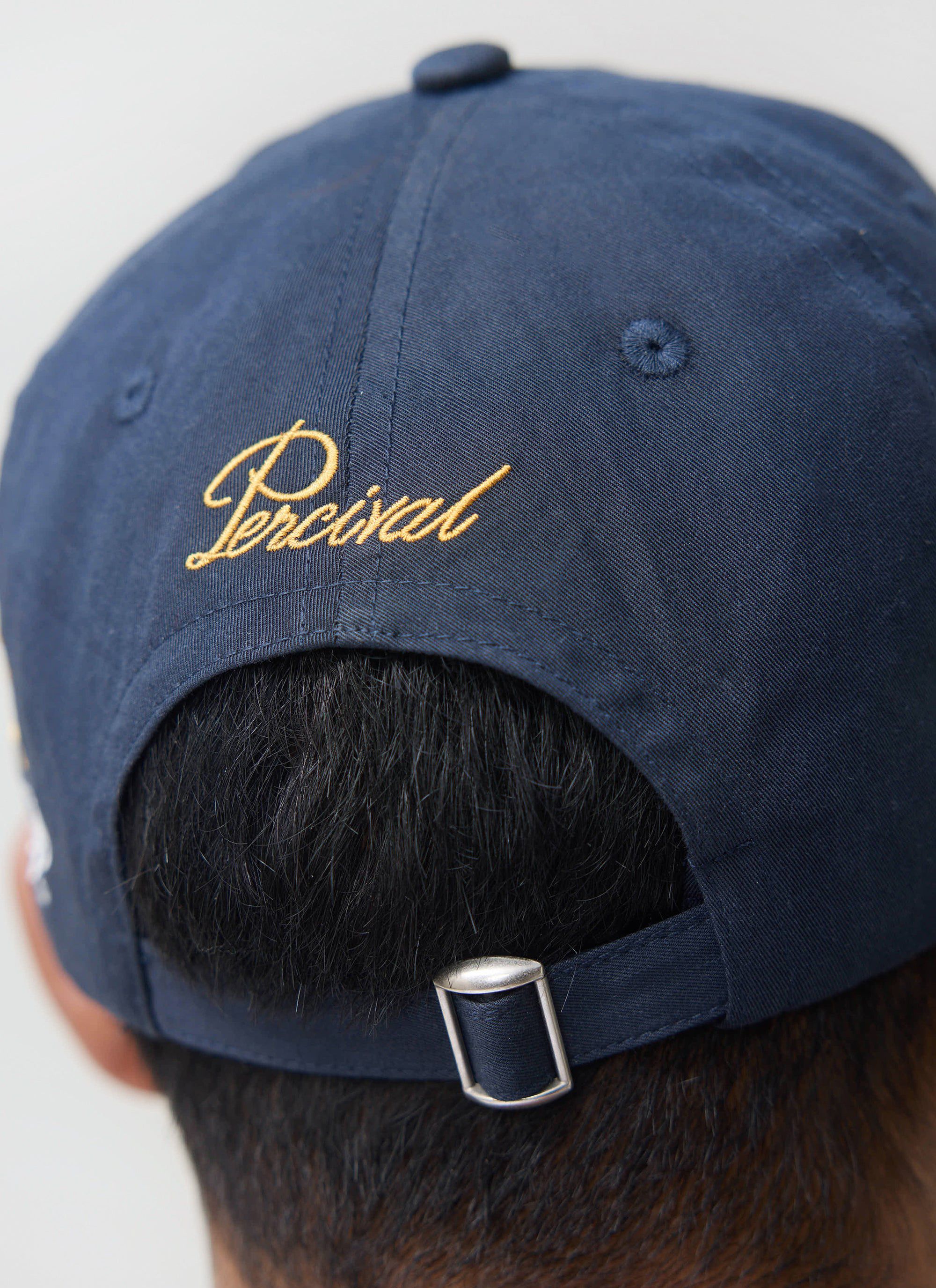 Close-up of the back of a model wearing the navy Guinness x Percival cap, showing the gold embroidered Percival logo.