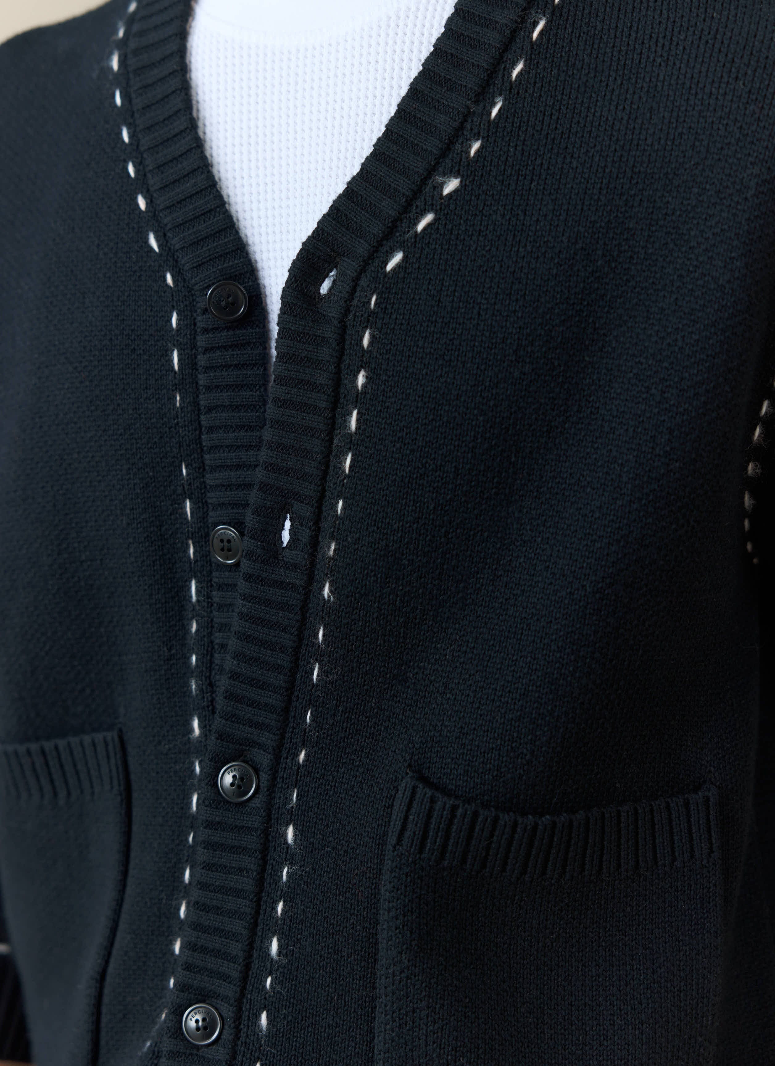 Close-up of the black Percival Module Boxy Cardigan showing the button front, pockets, and white stitch detailing.