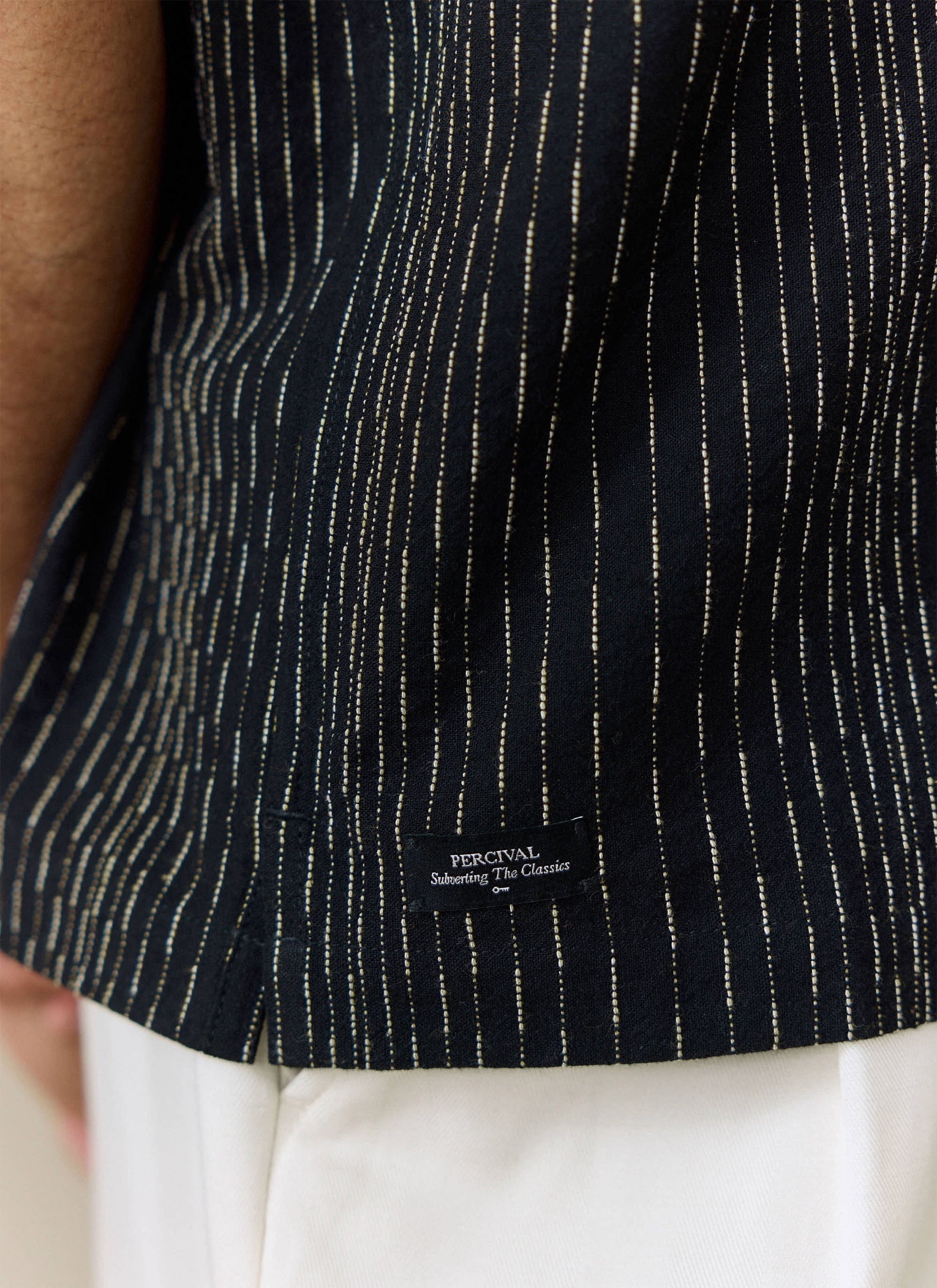 A close-up of the black Leland Cuban Shirt from Percival, showing the fabric detail and brand label at the hem.