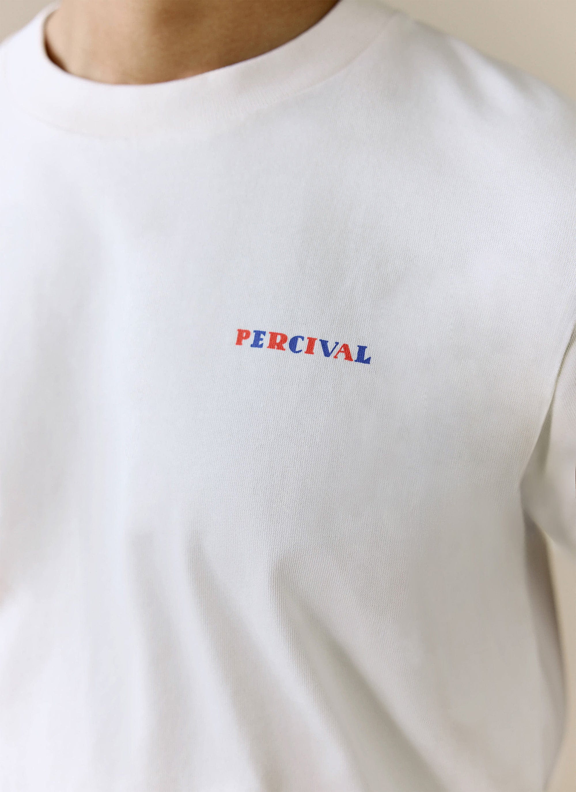 A close-up of the chest of the ecru Mixologist Martini T-Shirt, showing the red and blue Percival logo print.