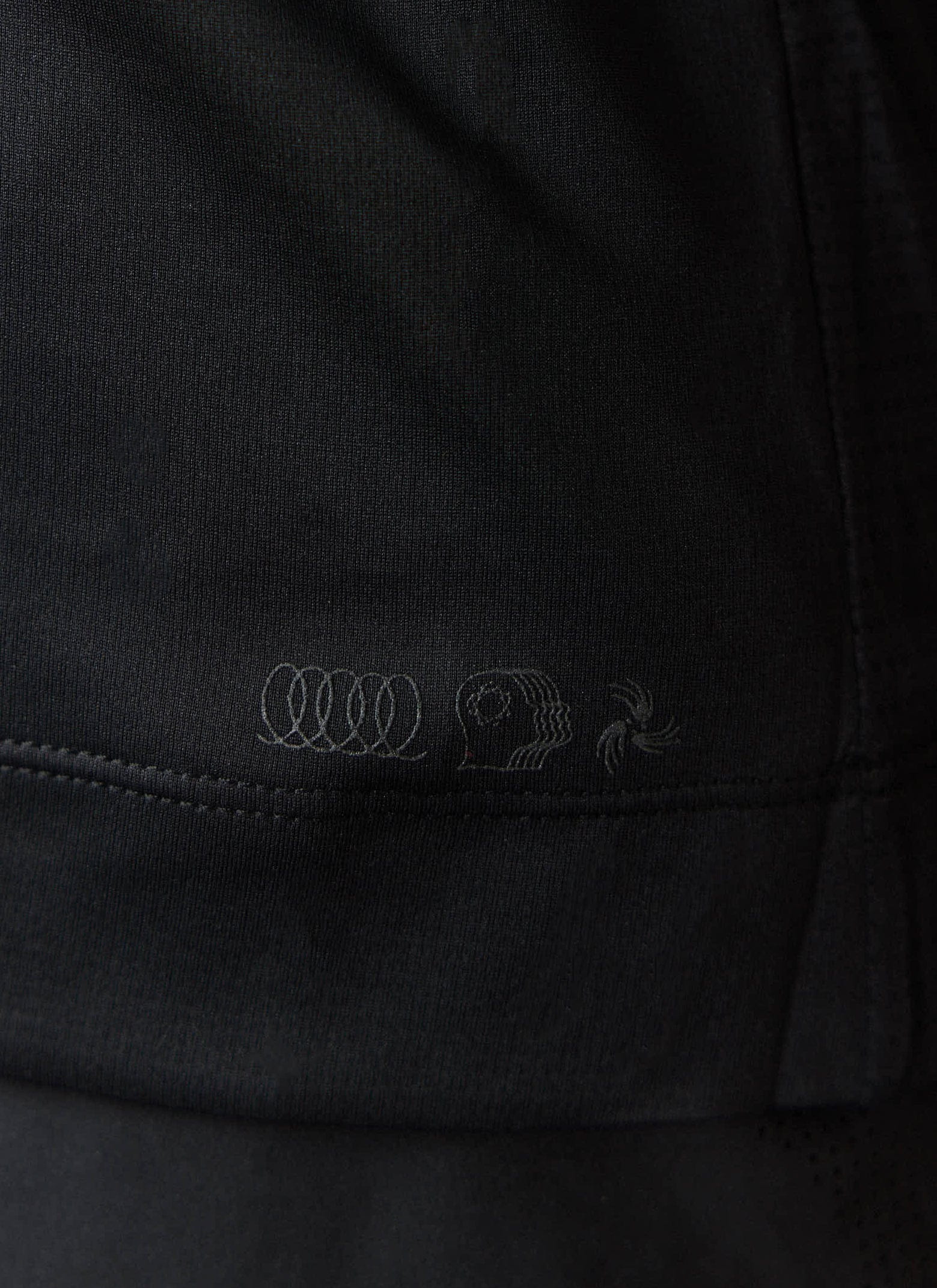 A close-up of the tonal PCVL artwork on the hem of the black Performance Vest by Percival.