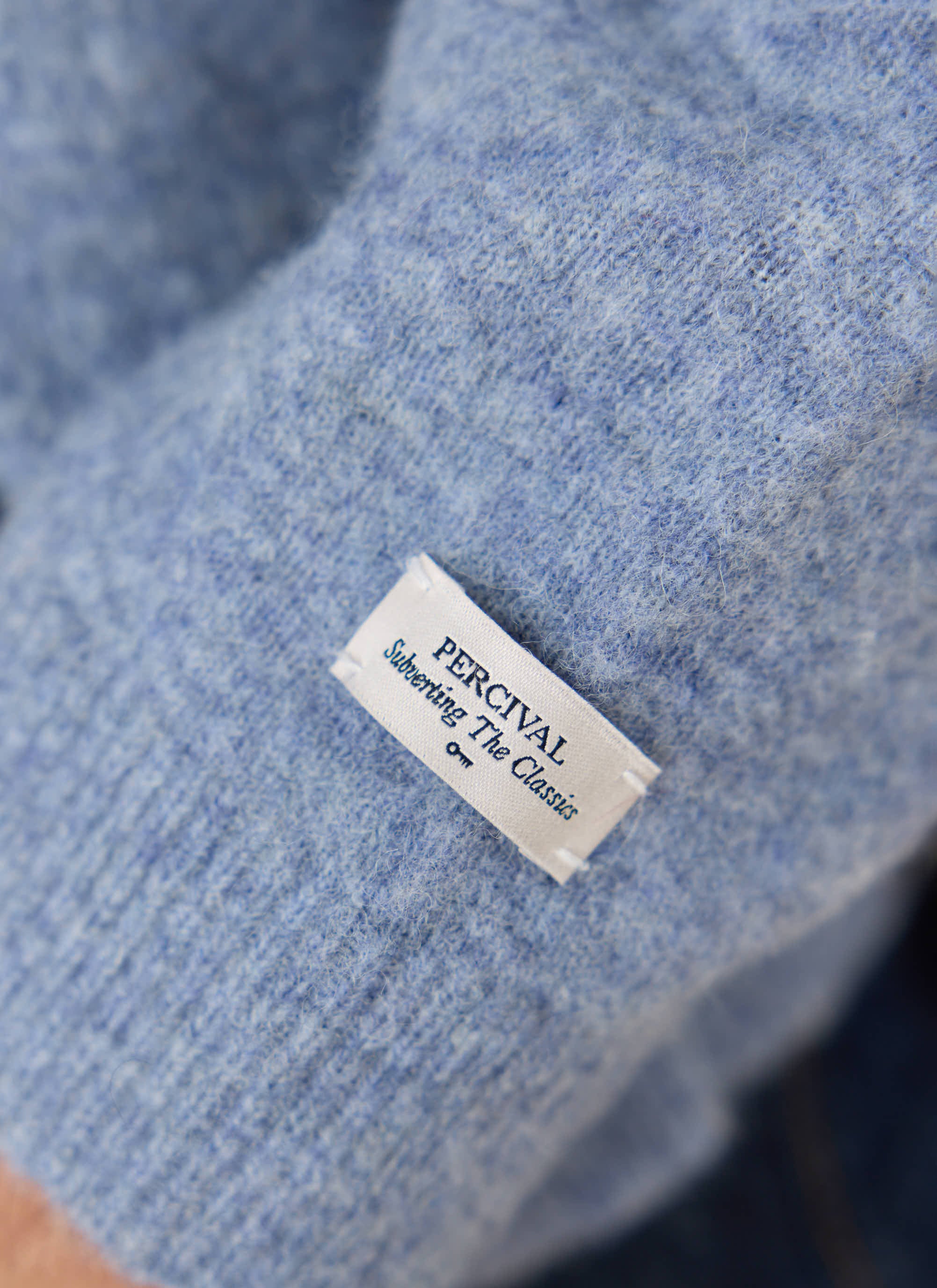 Close-up of the white Percival label on the soft heather blue yak wool fabric of the Archive Knitted Cardigan.