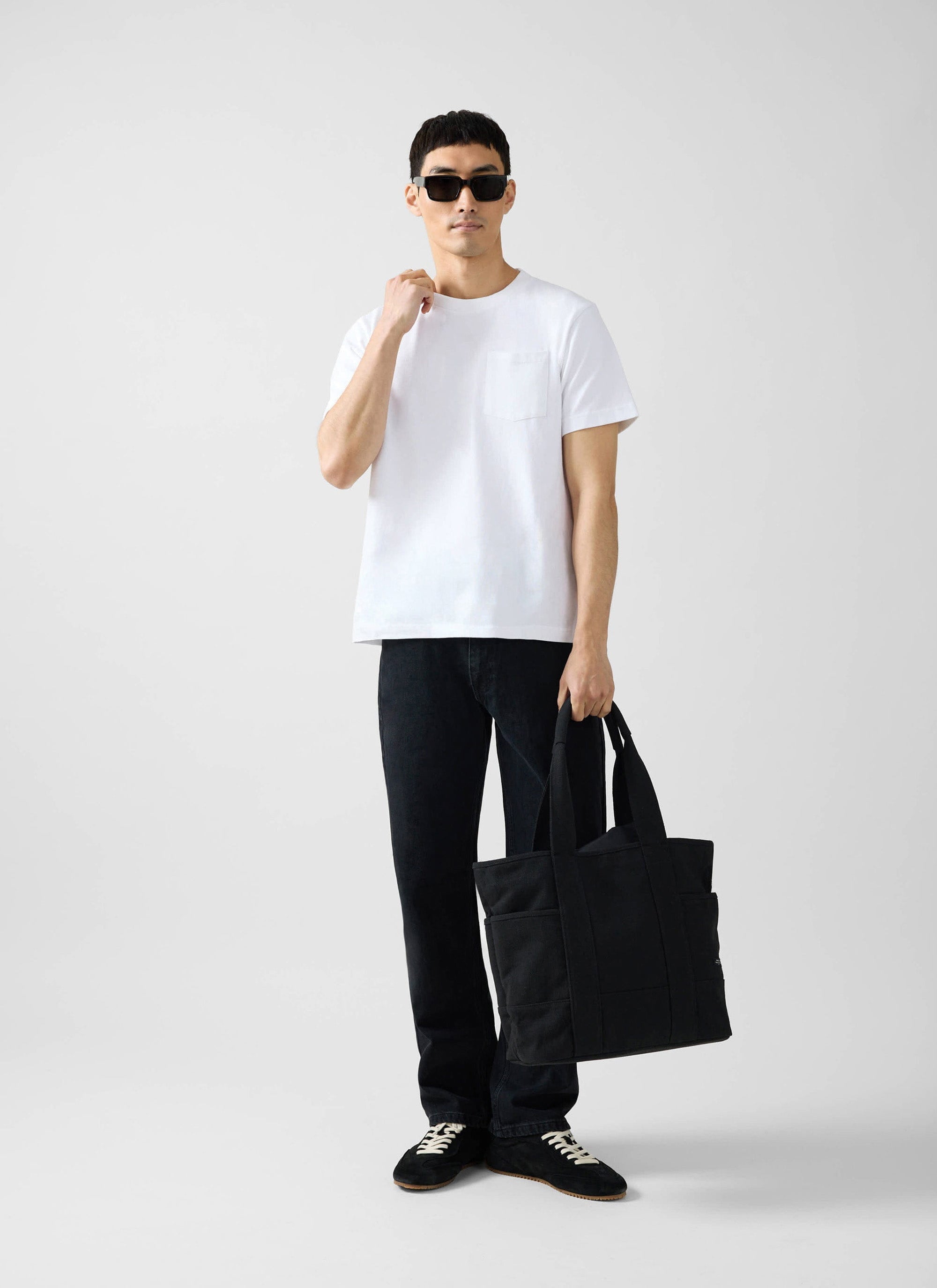 A model wears the white organic cotton Pocket T Shirt from Percival with black jeans, sunglasses, and a black tote bag.