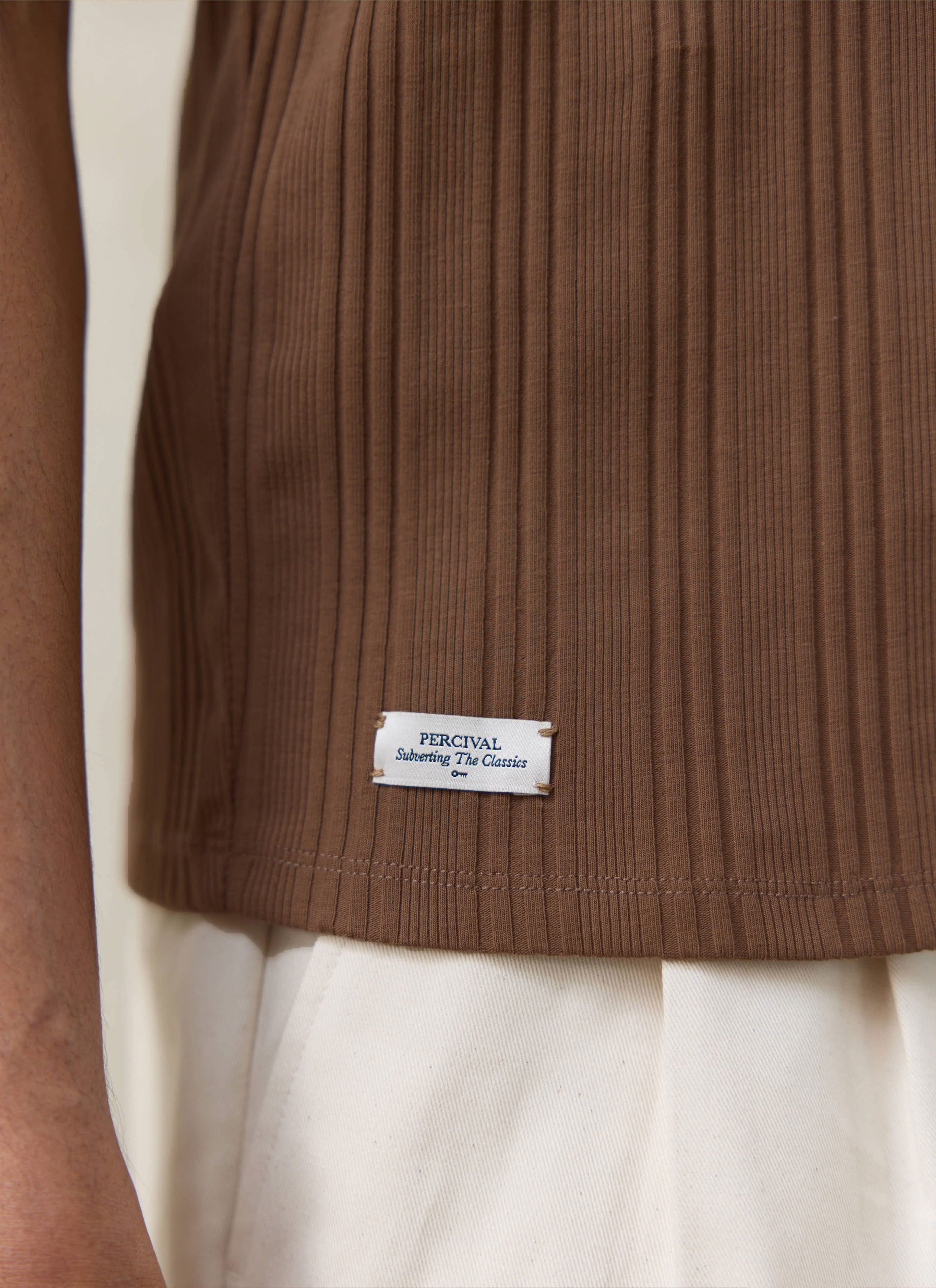 Close-up of the brown Percival Leon Ribbed Vest hem, showing the vertical organic cotton ribbing and woven brand label.