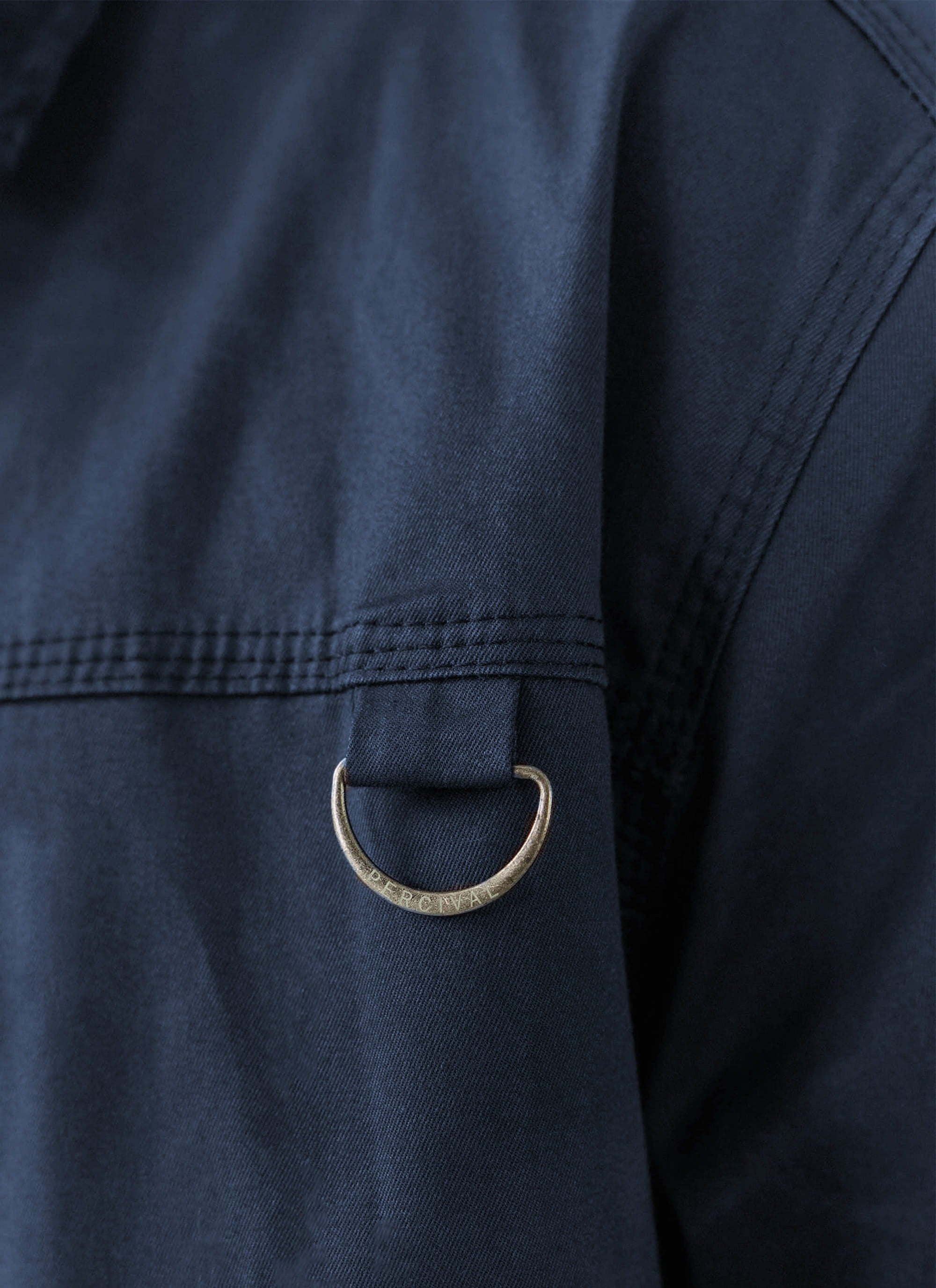 Detailed shot of the engraved metal D-ring on the navy blue waxed cotton Percival Wax Zip Jacket with tonal stitching.