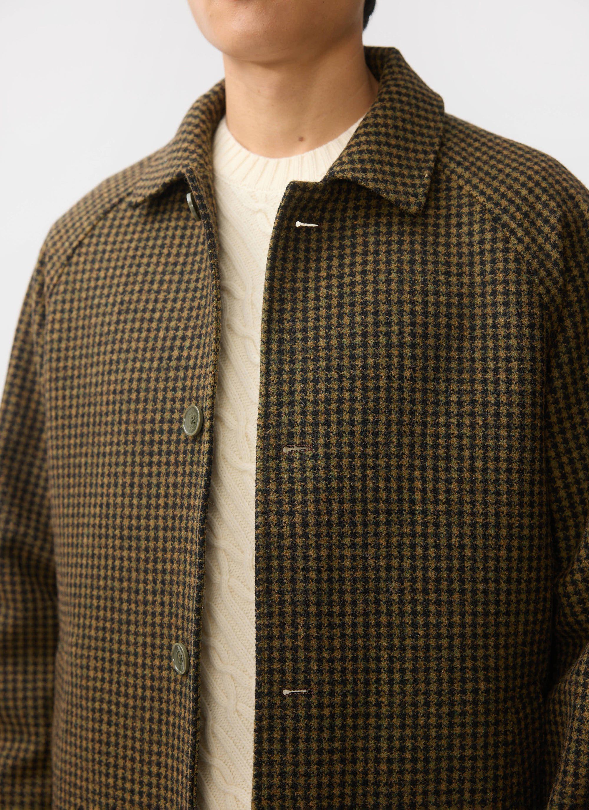 Close-up of a model wearing the Percival Dickens Car Coat in brown houndstooth check over a cream cable-knit jumper.