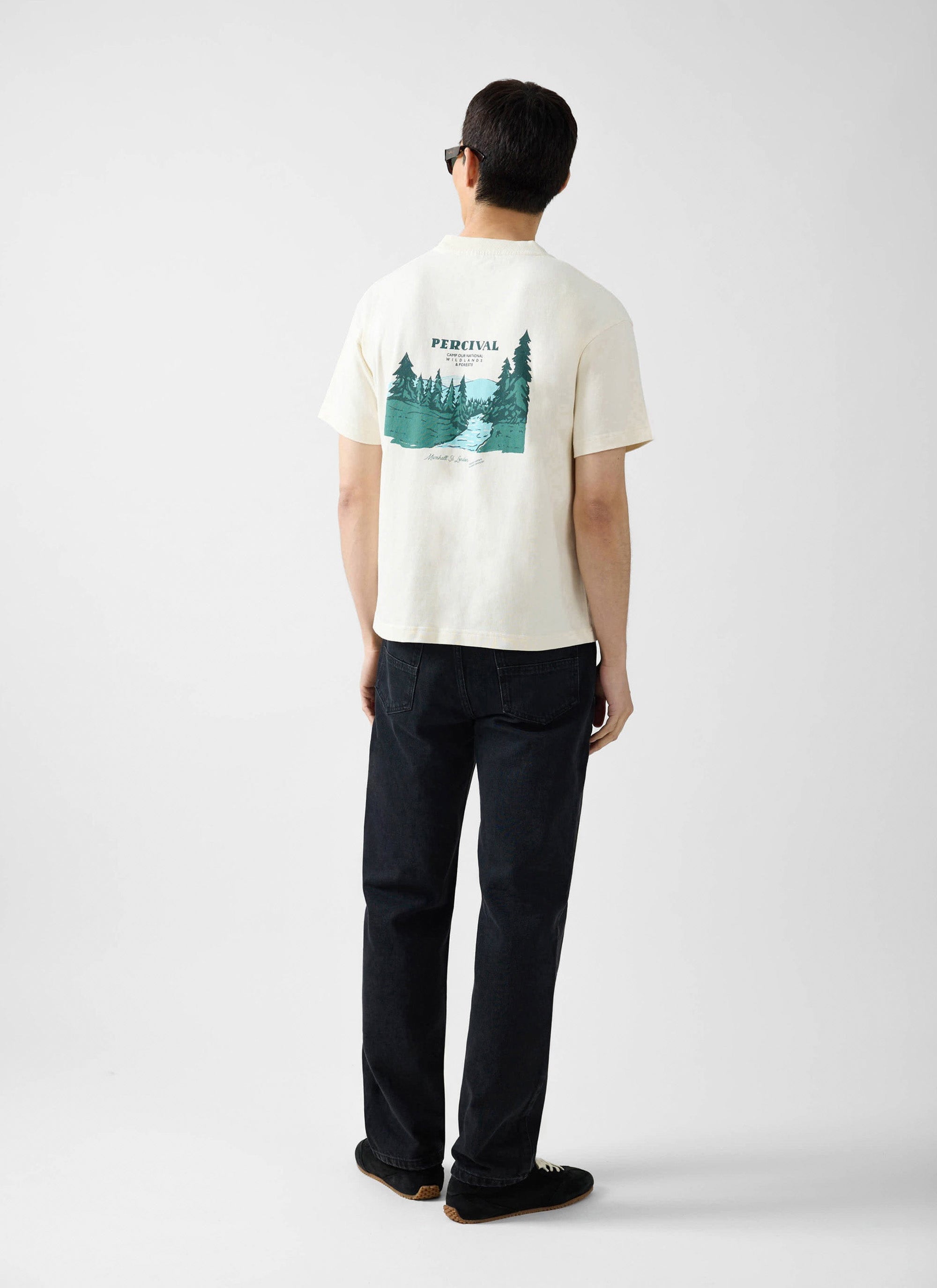 A man models the Percival Wildlands oversized t-shirt in ecru, showing the detailed graphic print on the back.