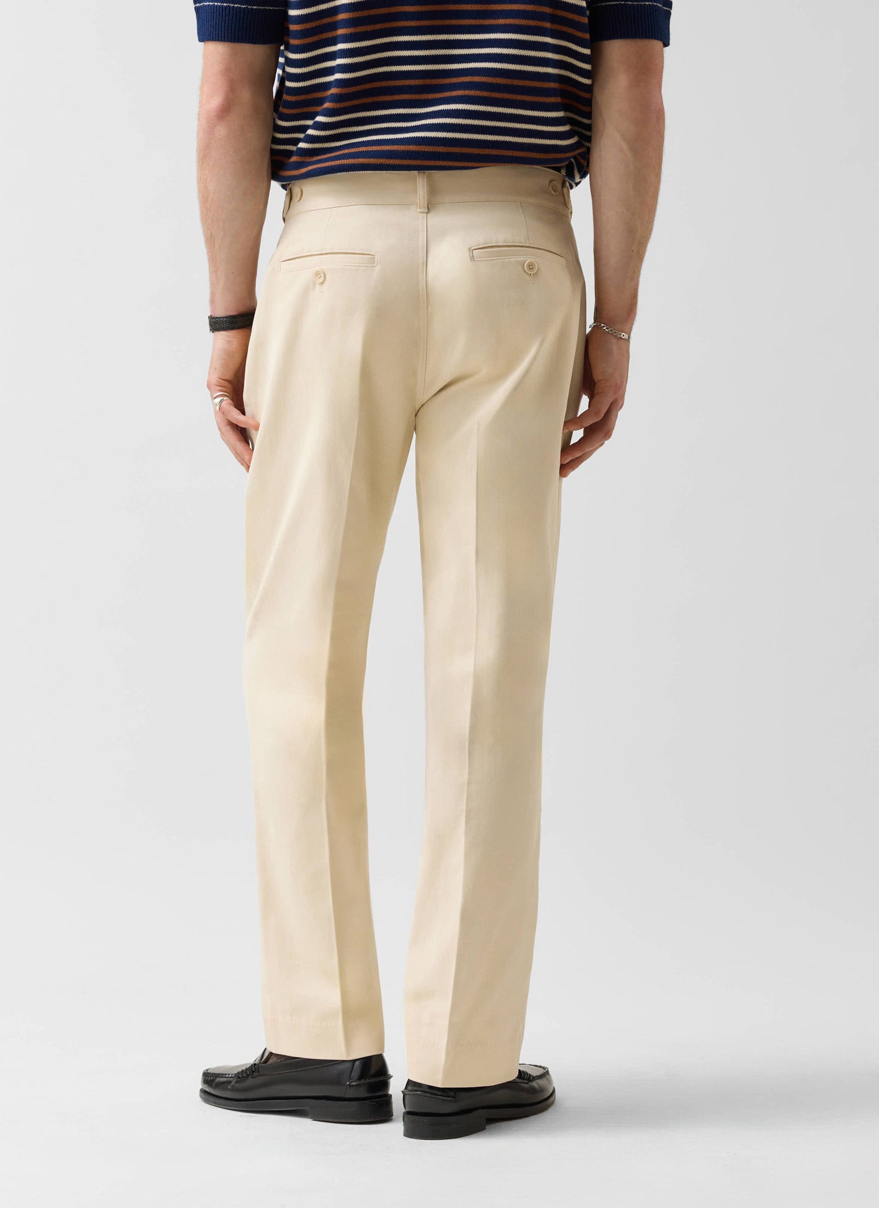 A rear view of a model wearing the Percival Straight Leg Chino in ecru, paired with a striped polo and loafers.