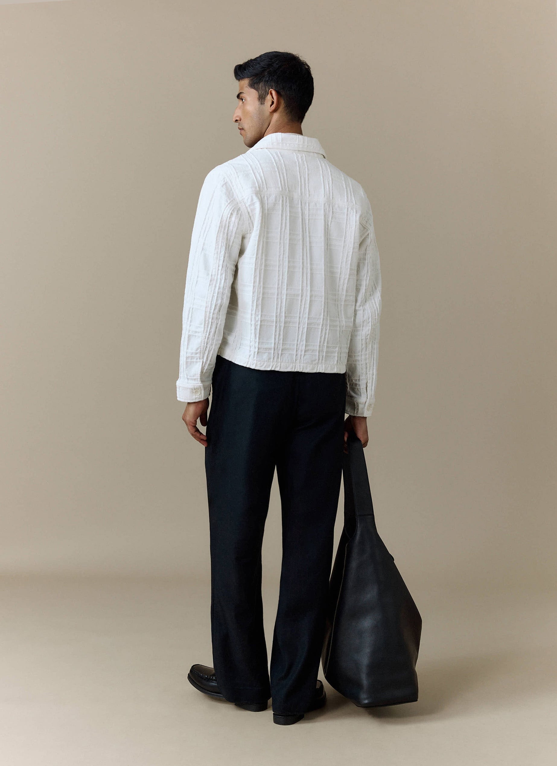 A model, shot from behind, wears the Percival Canyon Heavyweight Overshirt in ecru with black trousers and a black bag.