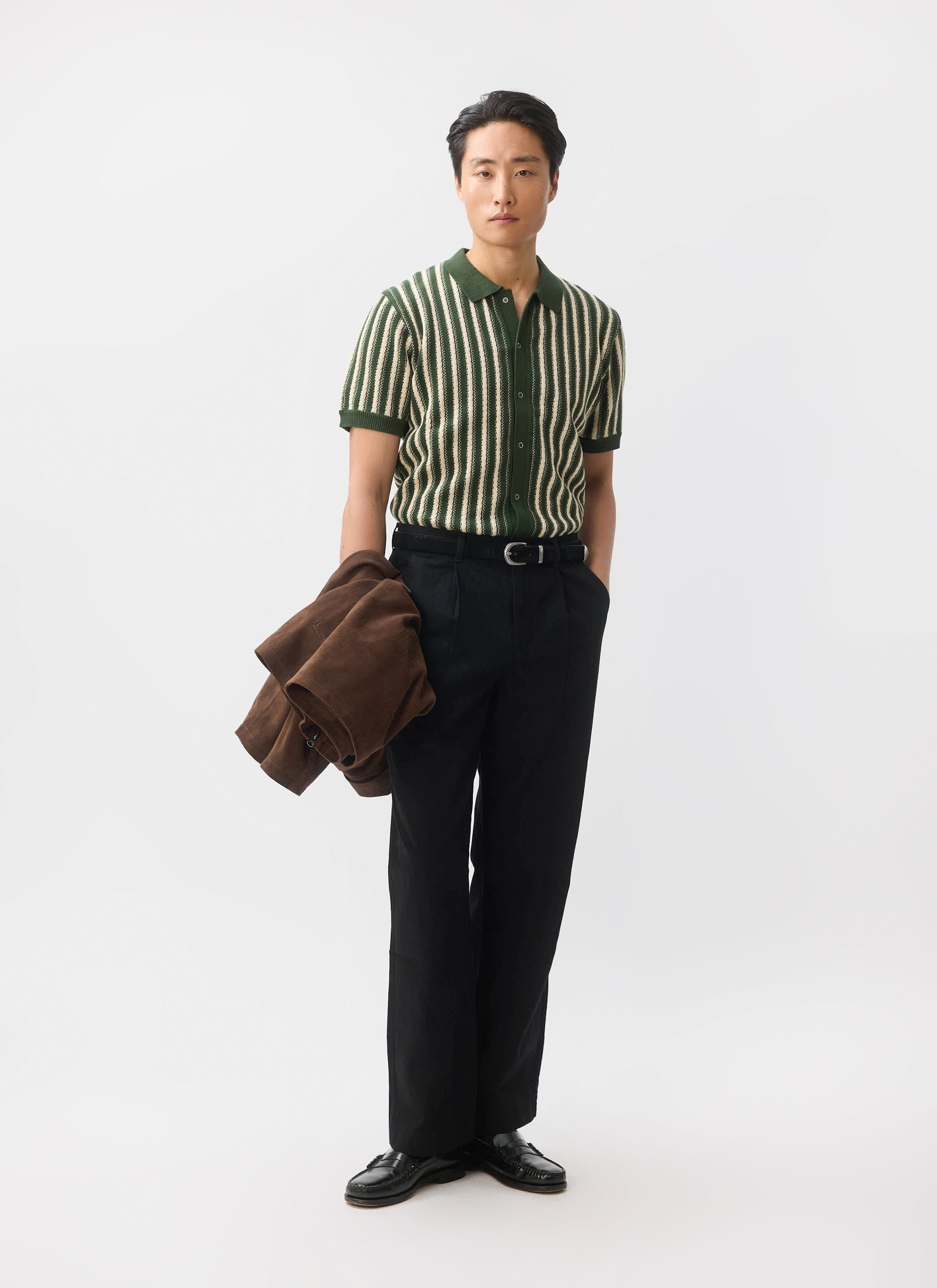 A model wears the Percival Collins Knitted Shirt in green with vertical stripes, paired with black trousers and loafers.