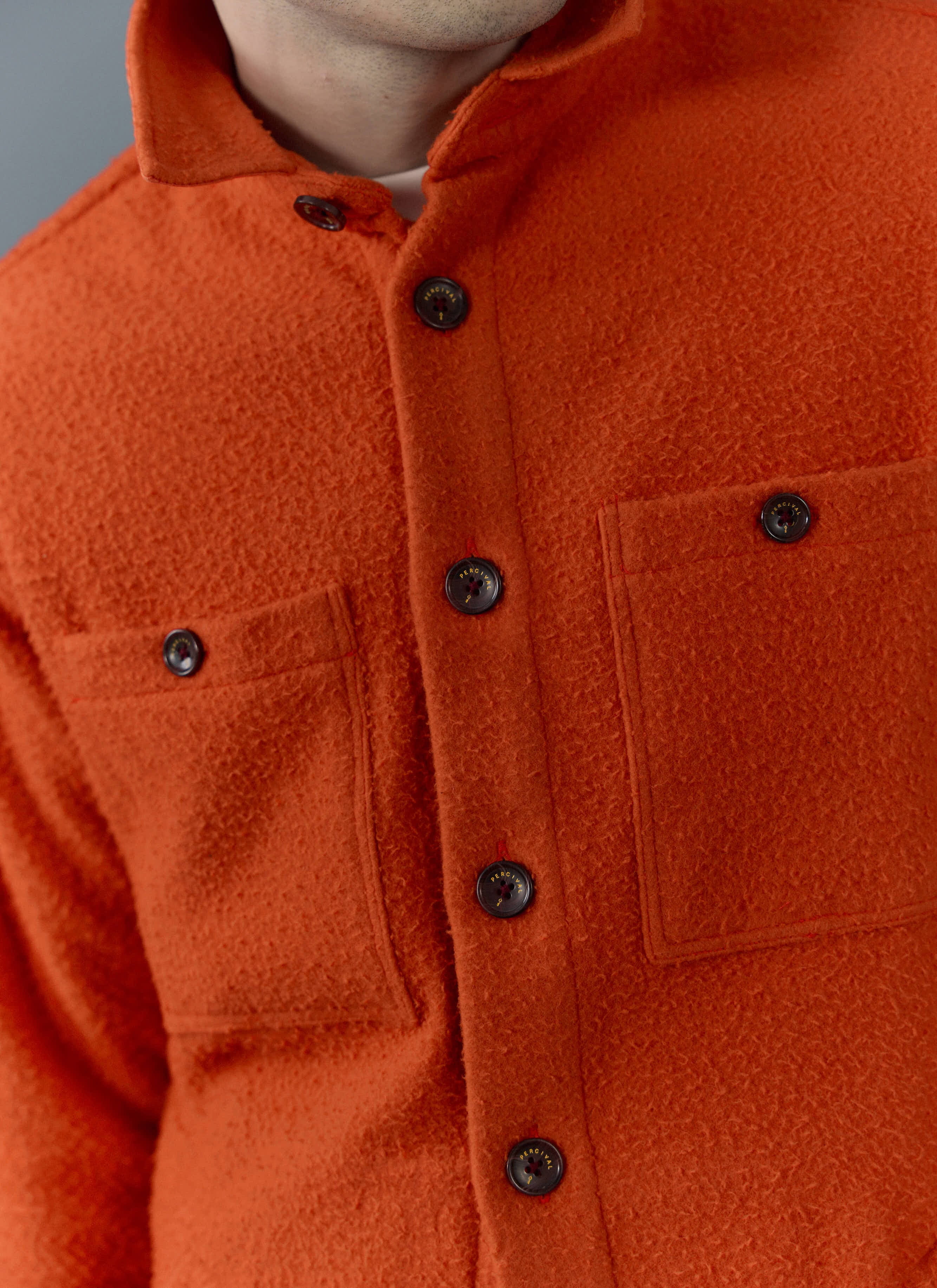 Close up of the orange Percival Blanket Overshirt in Casentino wool, showing the textured fabric and branded buttons.